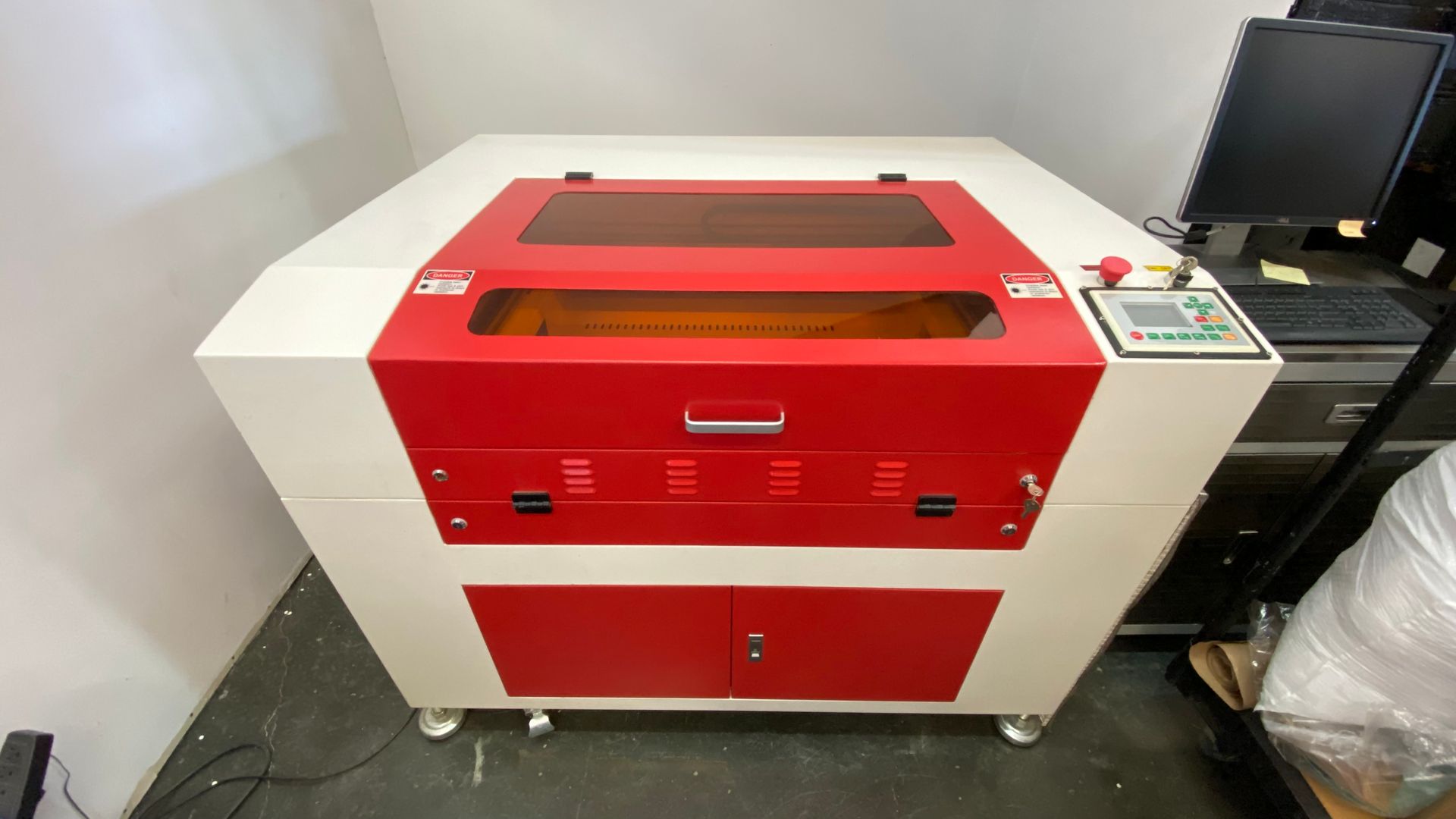 Used QX-60-9060 CO2 laser cutting and engraving machine with red and white enclosed cabinet, front access door, viewing window, and side-mounted control panel.