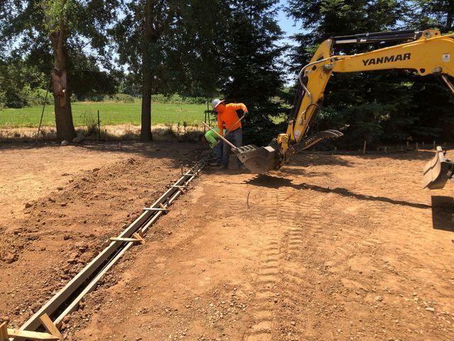 Man is Digging in the Dirt Next to a Yellow Excavator – Elk Grove, CA – AVM Concrete