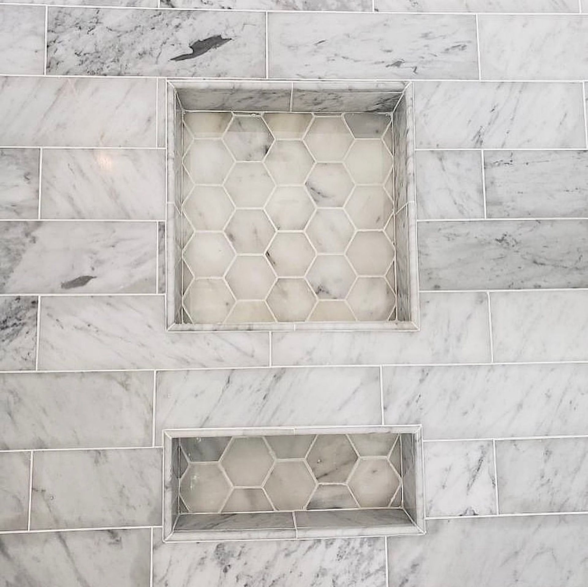Marble tiled shower with two recessed shelves, each containing hexagonal tile.
