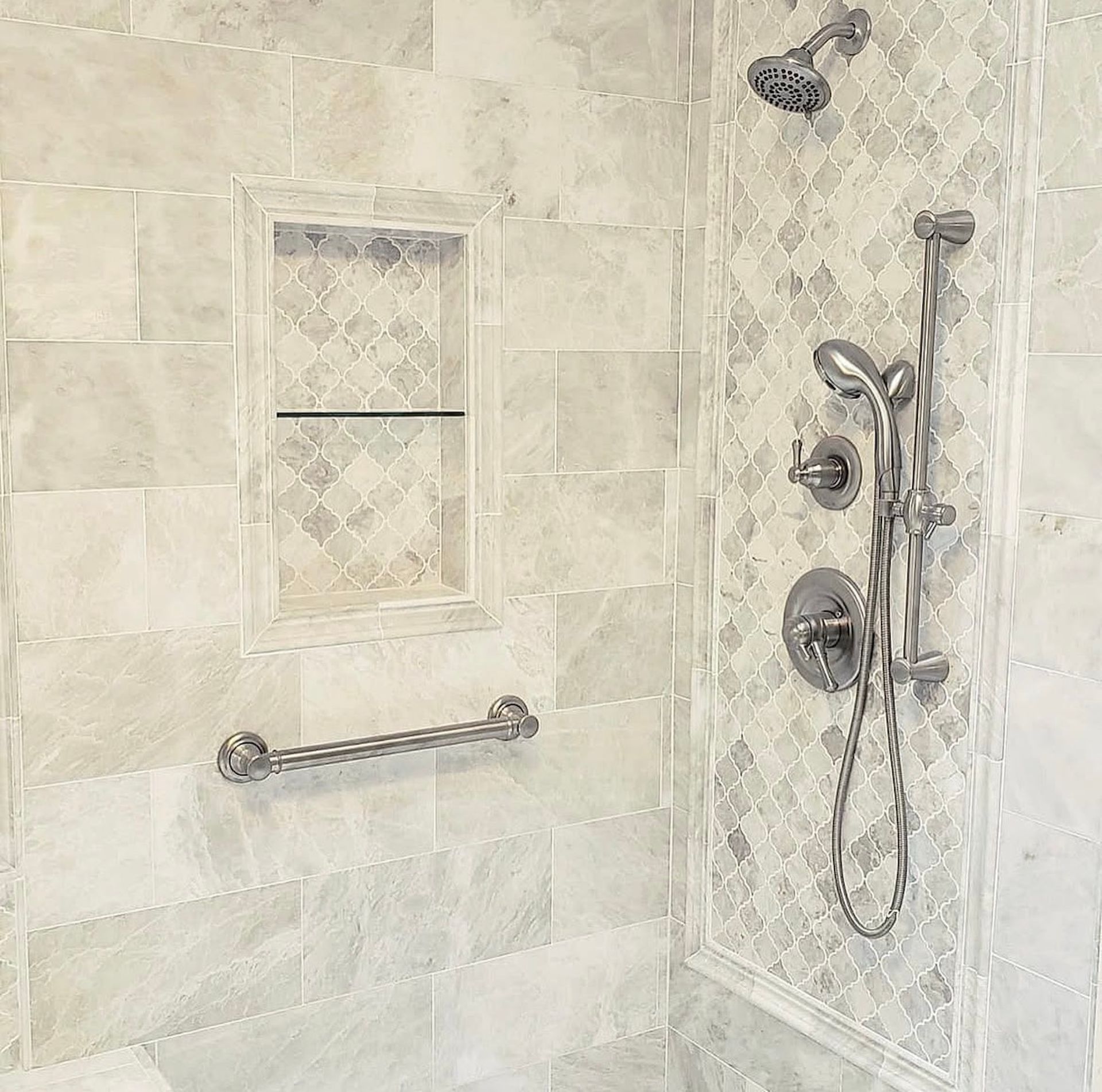 Bathroom shower with marble tiles, a built-in shelf, grab bar, and shower fixtures.