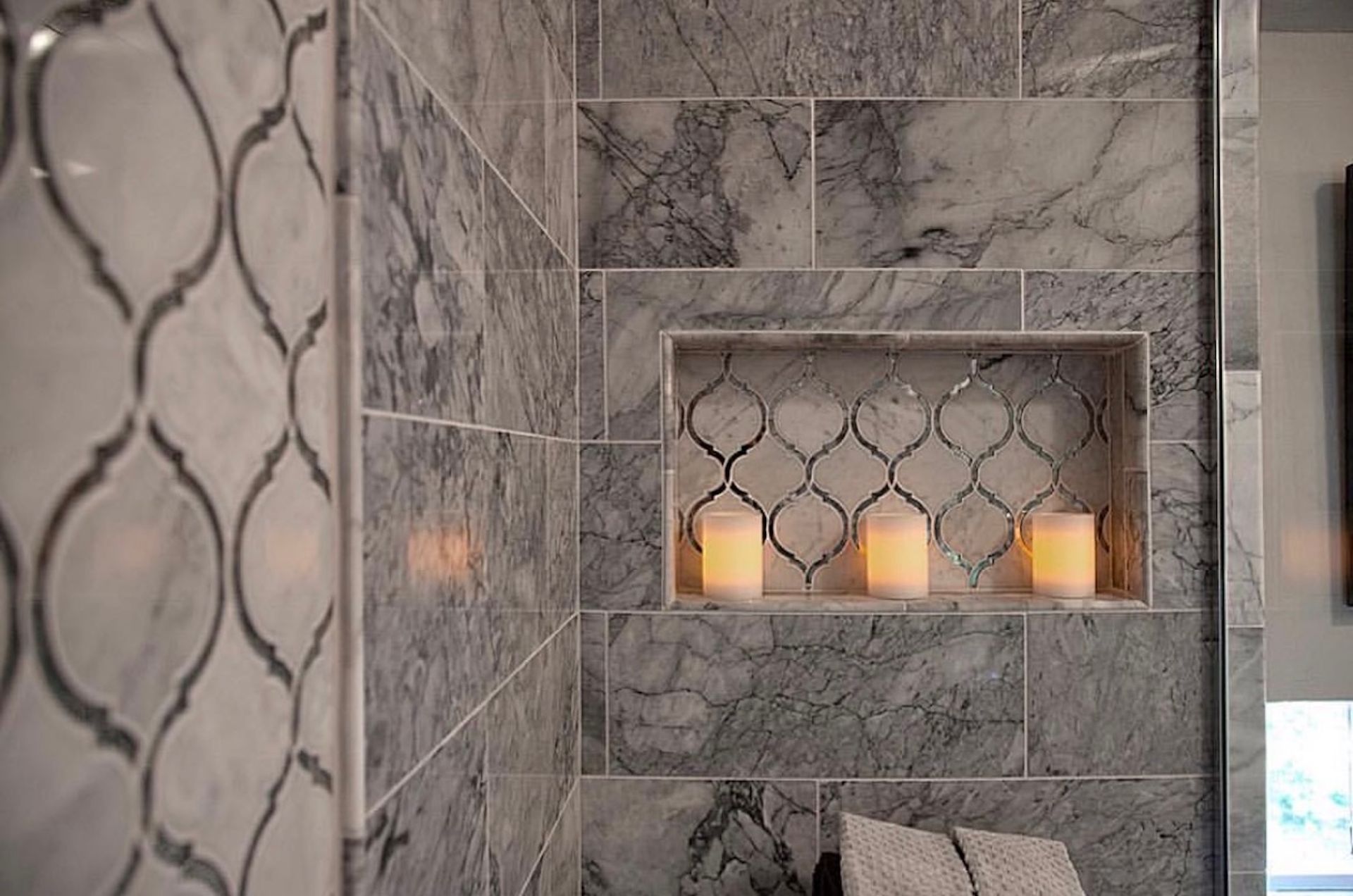 Bathroom shower with gray marble tile and decorative niche with candles.
