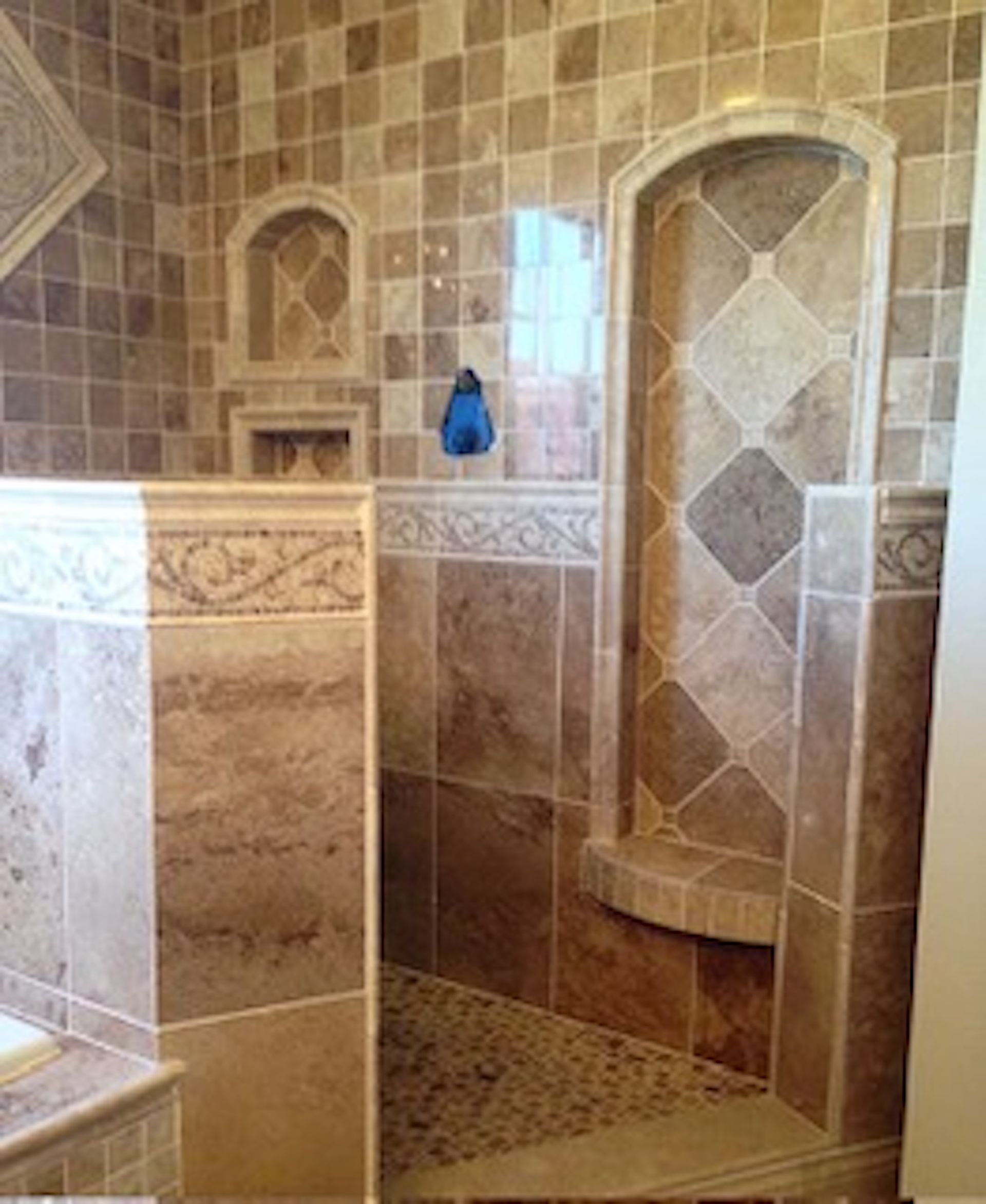 Tiled bathroom shower with a built-in arched shelf, in shades of brown and tan.