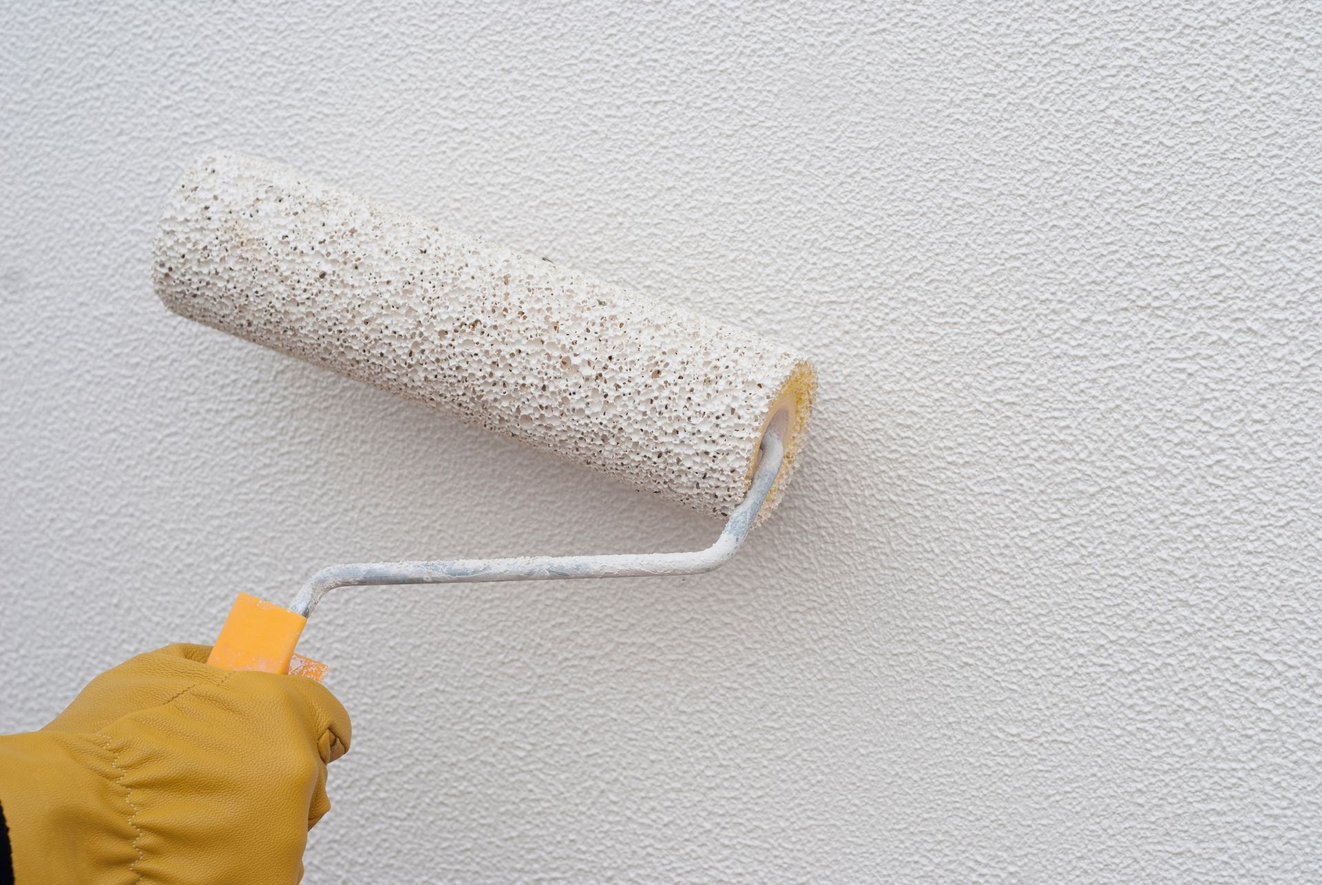 Hand holding a paint roller applying white paint to a textured wall.