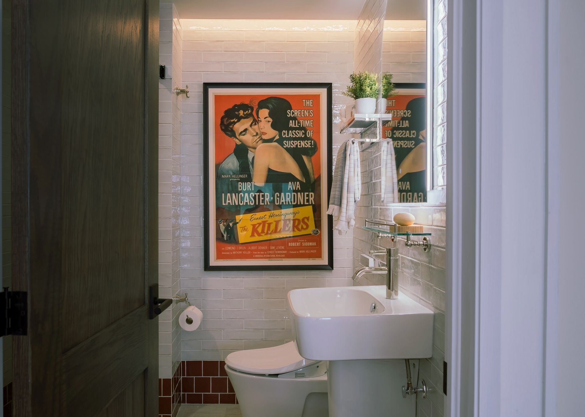 A bathroom with a toilet, sink, mirror and a poster on the wall.