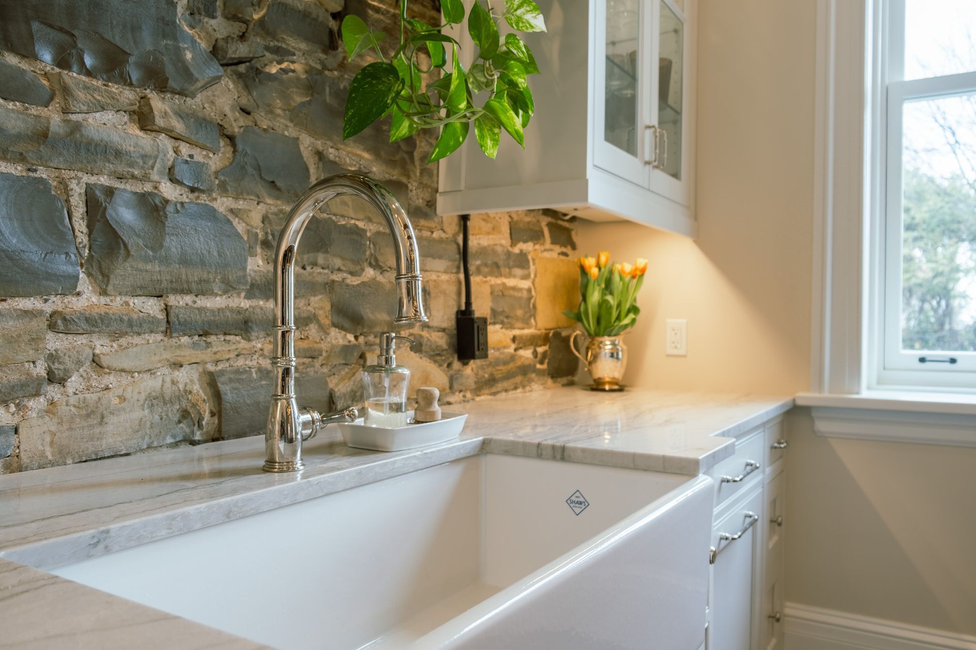 A kitchen sink with a faucet and a brick wall behind it.