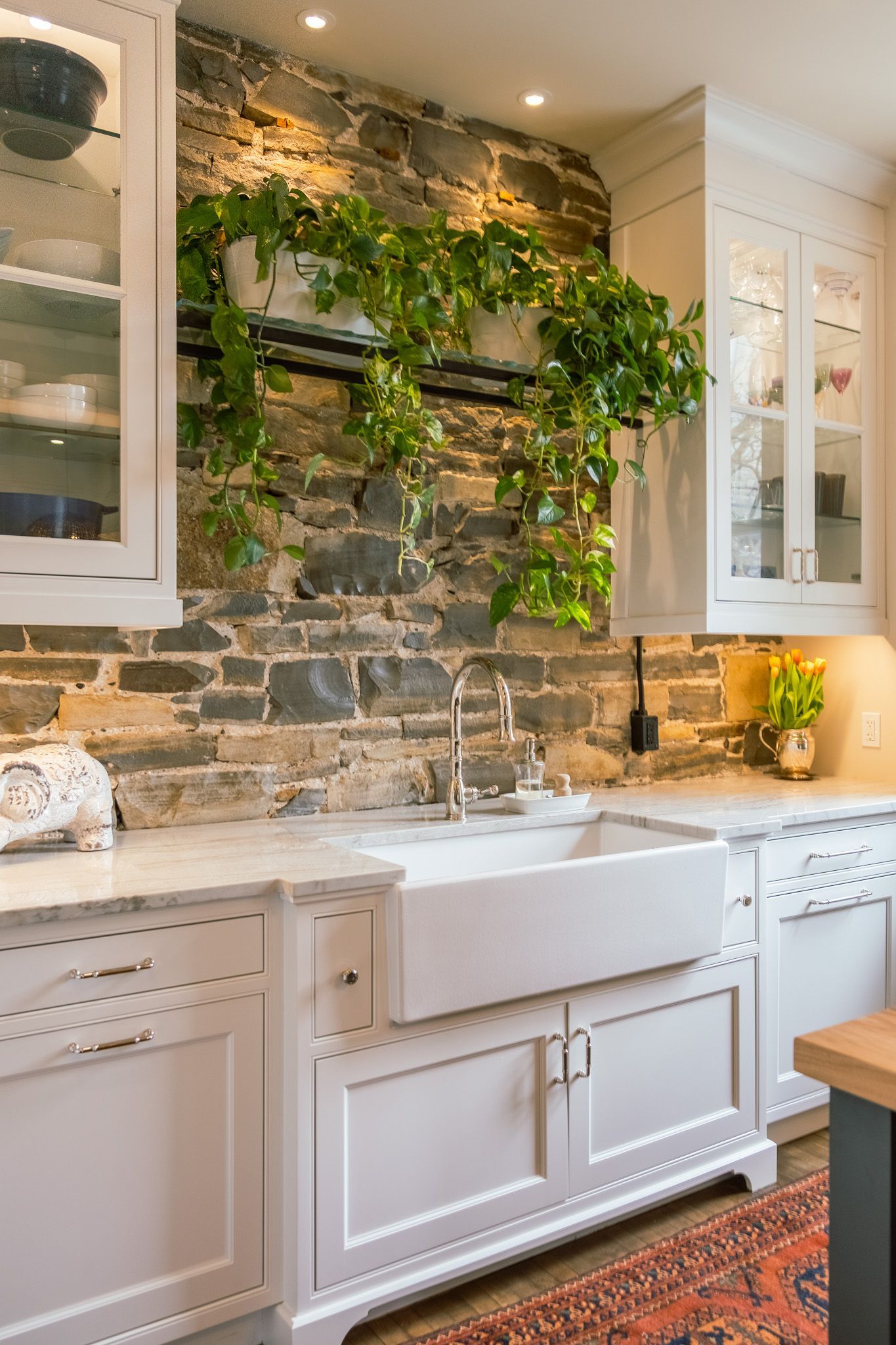 A kitchen with a sink, cabinets, and a stone wall.