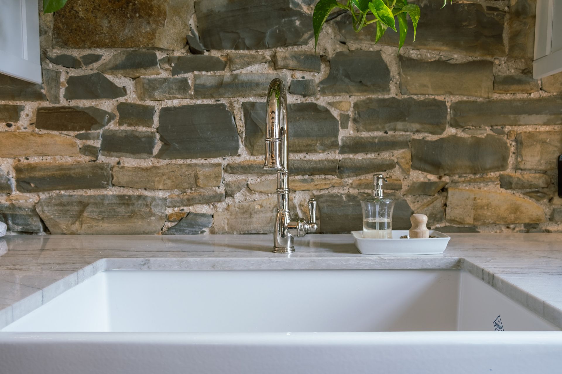 A kitchen sink sitting in front of a stone wall.