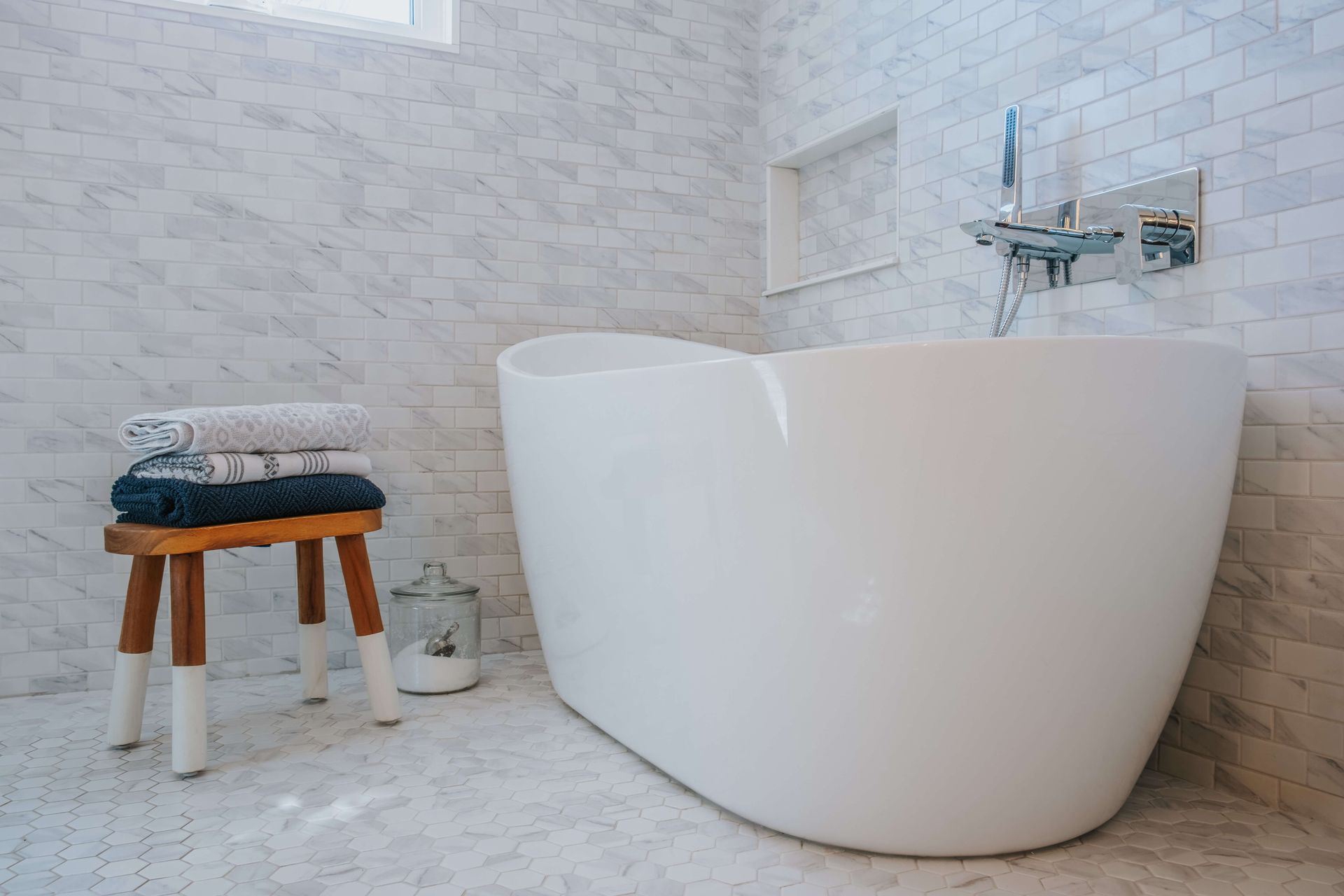 A bathroom with a bathtub and a stool with towels on it.