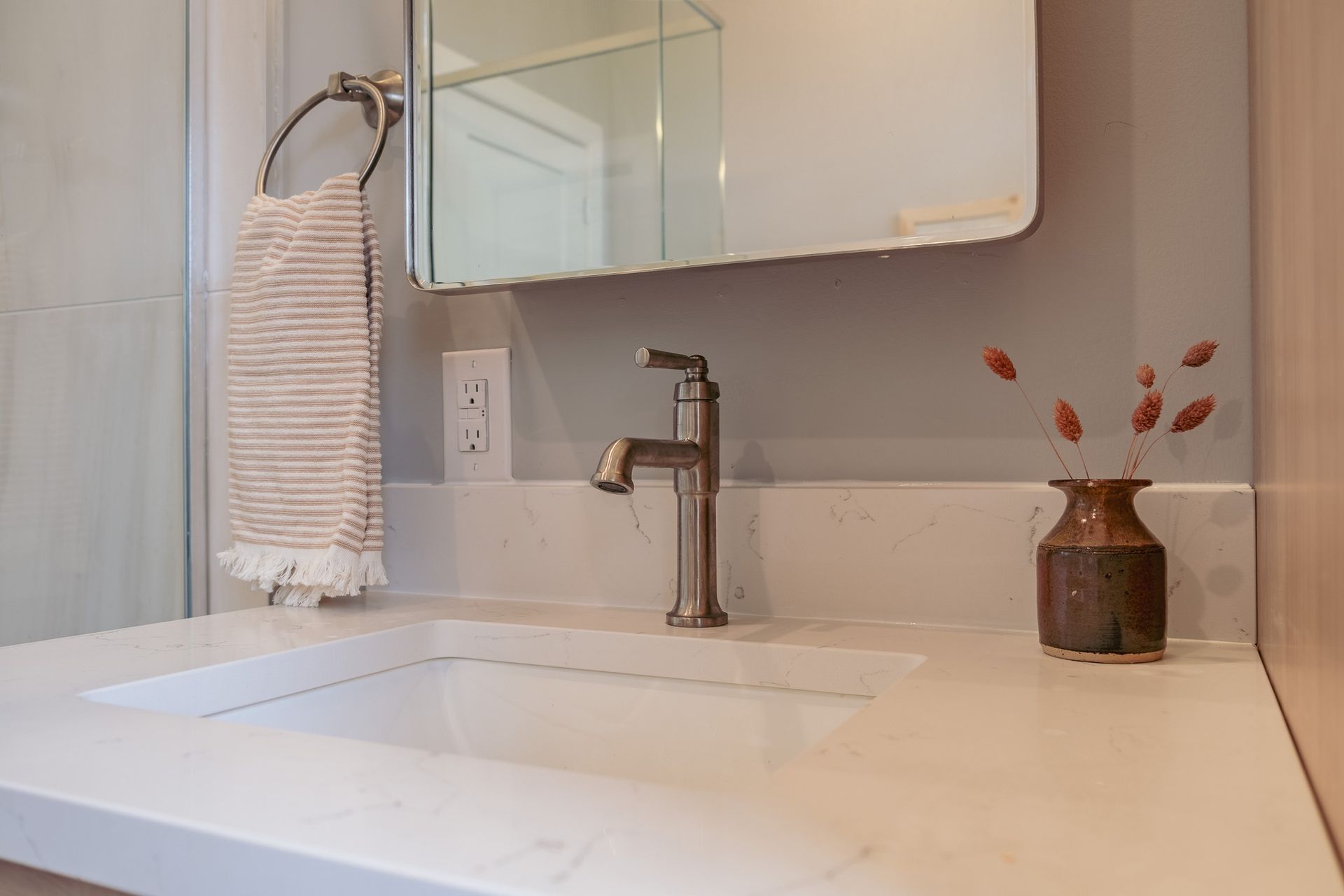 A bathroom sink with a mirror and a vase on the counter.