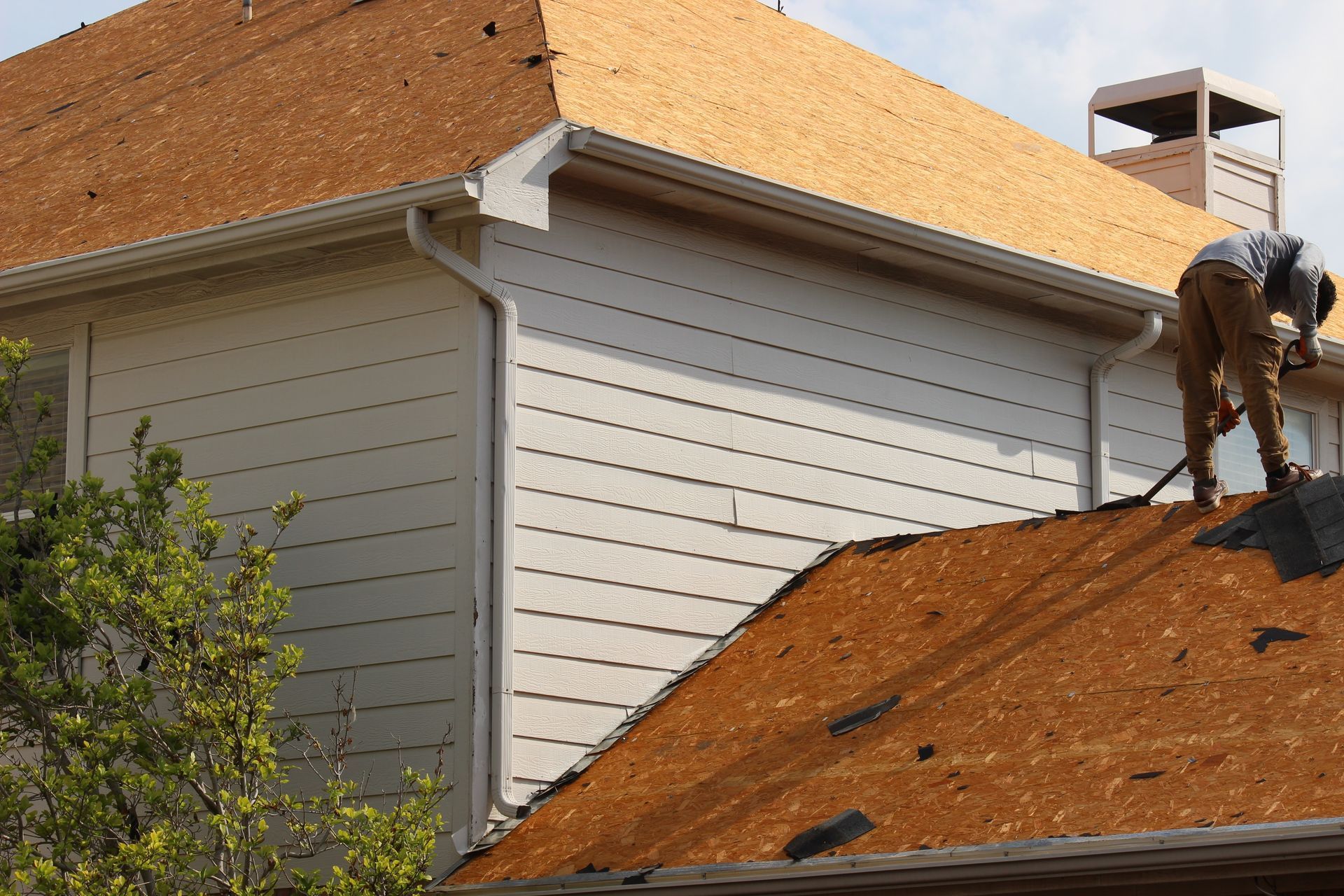 Roofer replacing shingles on a house with white siding and brown roof.