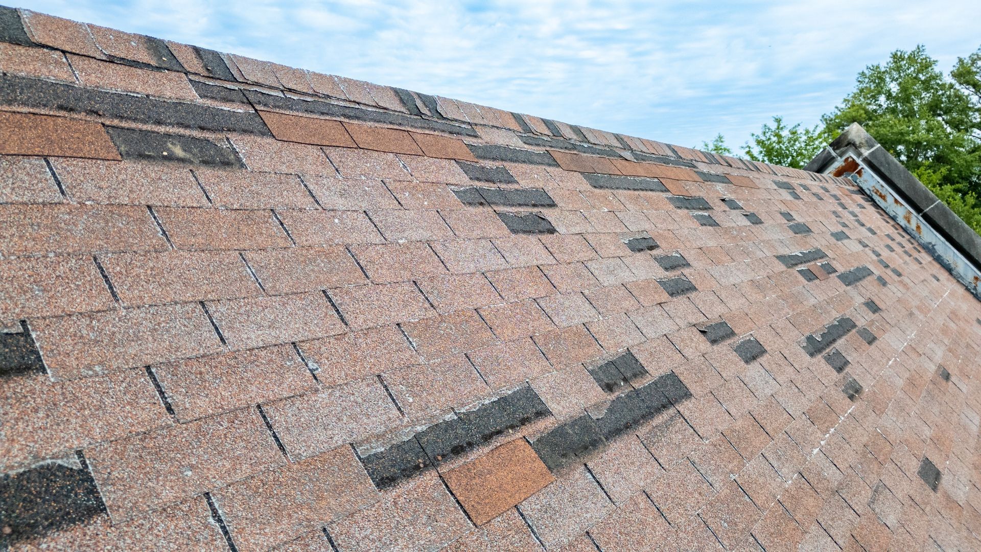 Damaged asphalt shingle roof with missing and broken shingles.