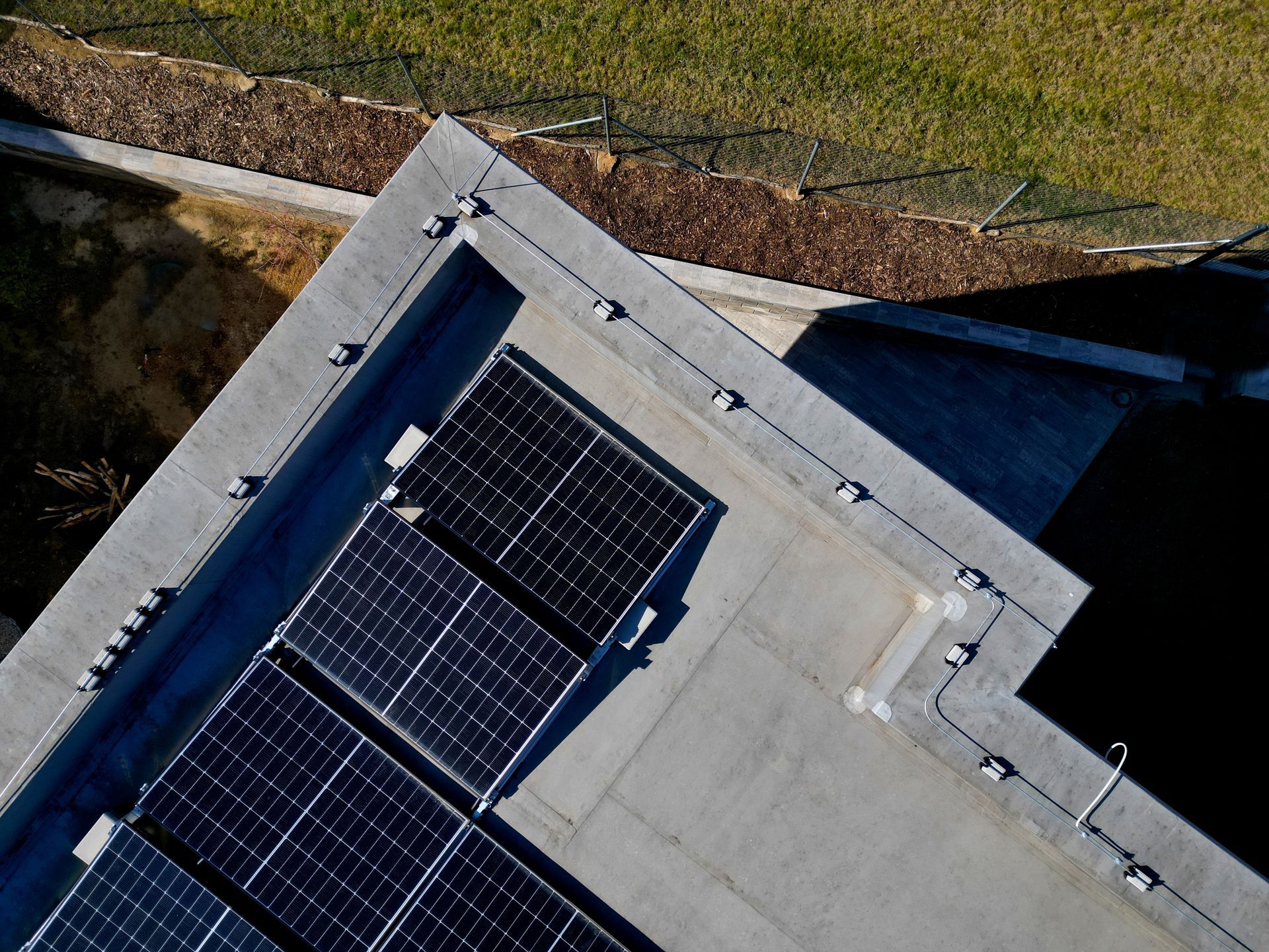 Overhead view of a concrete rooftop with solar panels. Adjacent to a grass field and a low fence.