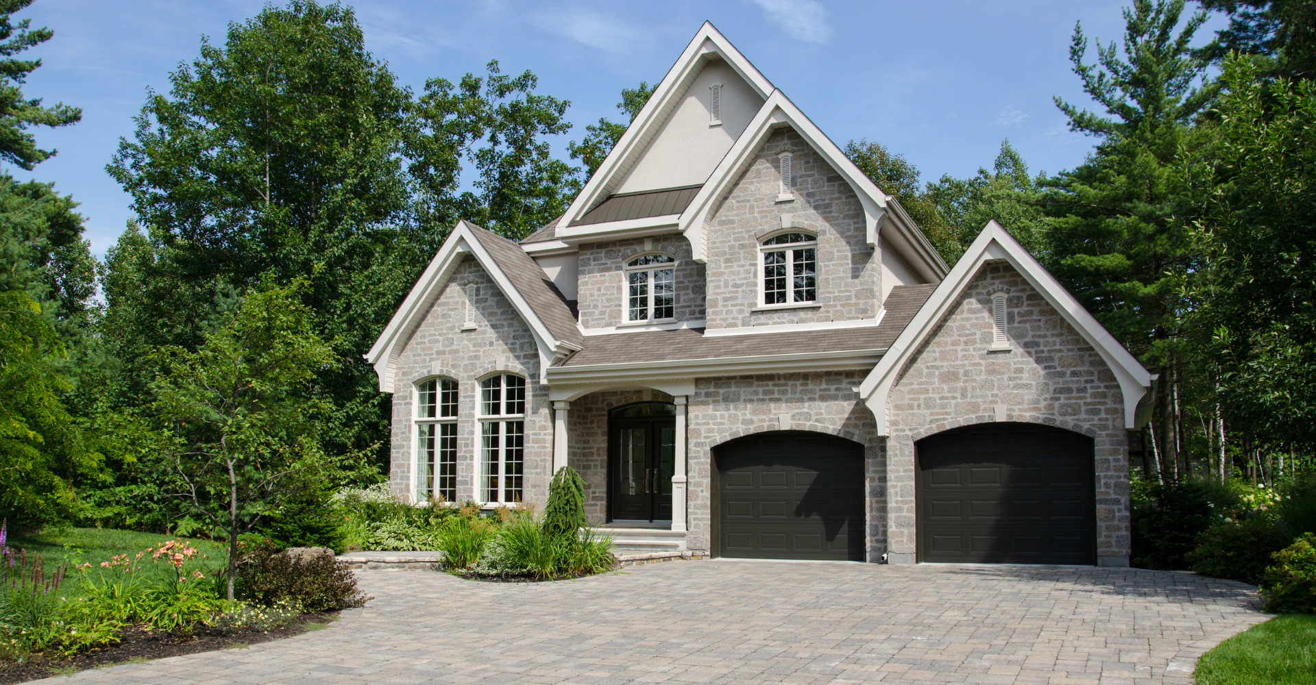 A large house with two black garage doors is surrounded by trees.