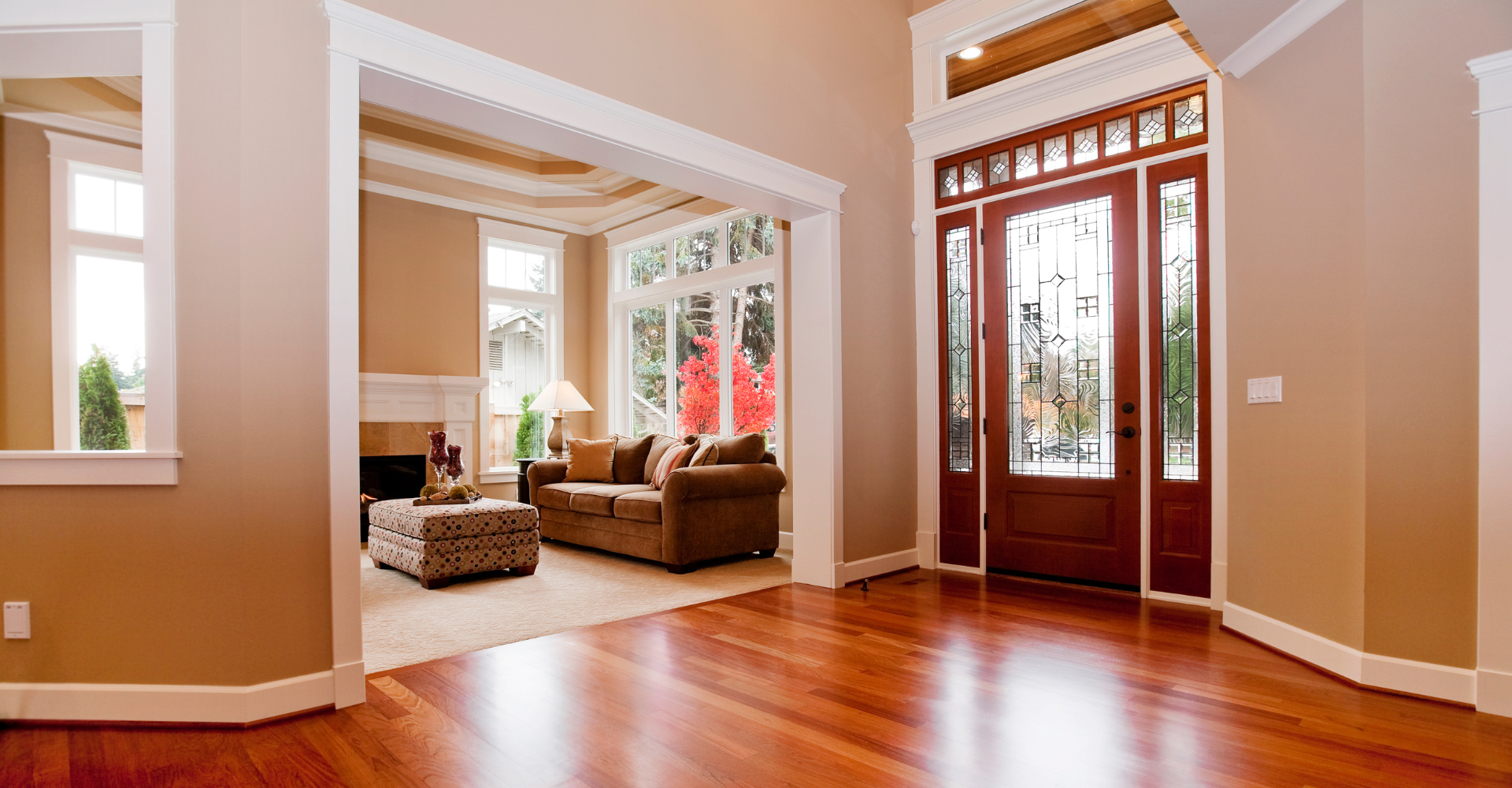 An empty living room with hardwood floors and a red door.