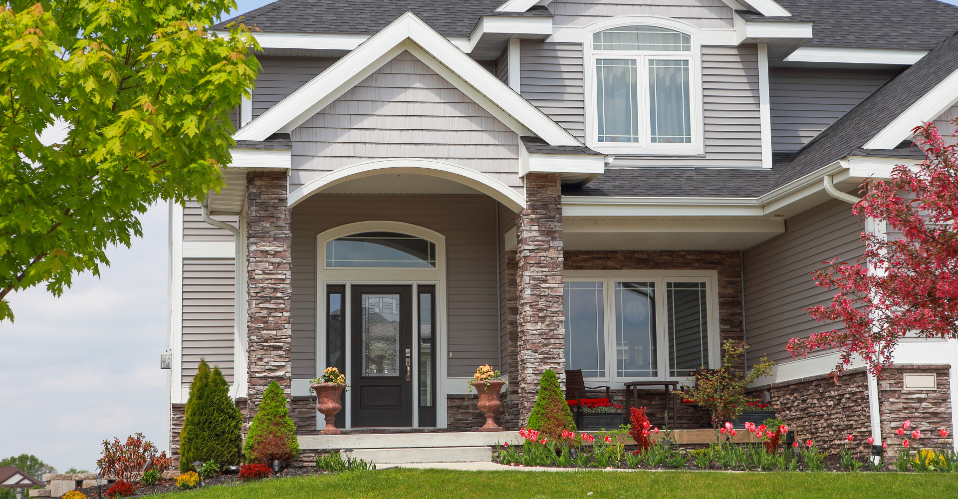 A large house with a large porch and a tree in front of it.