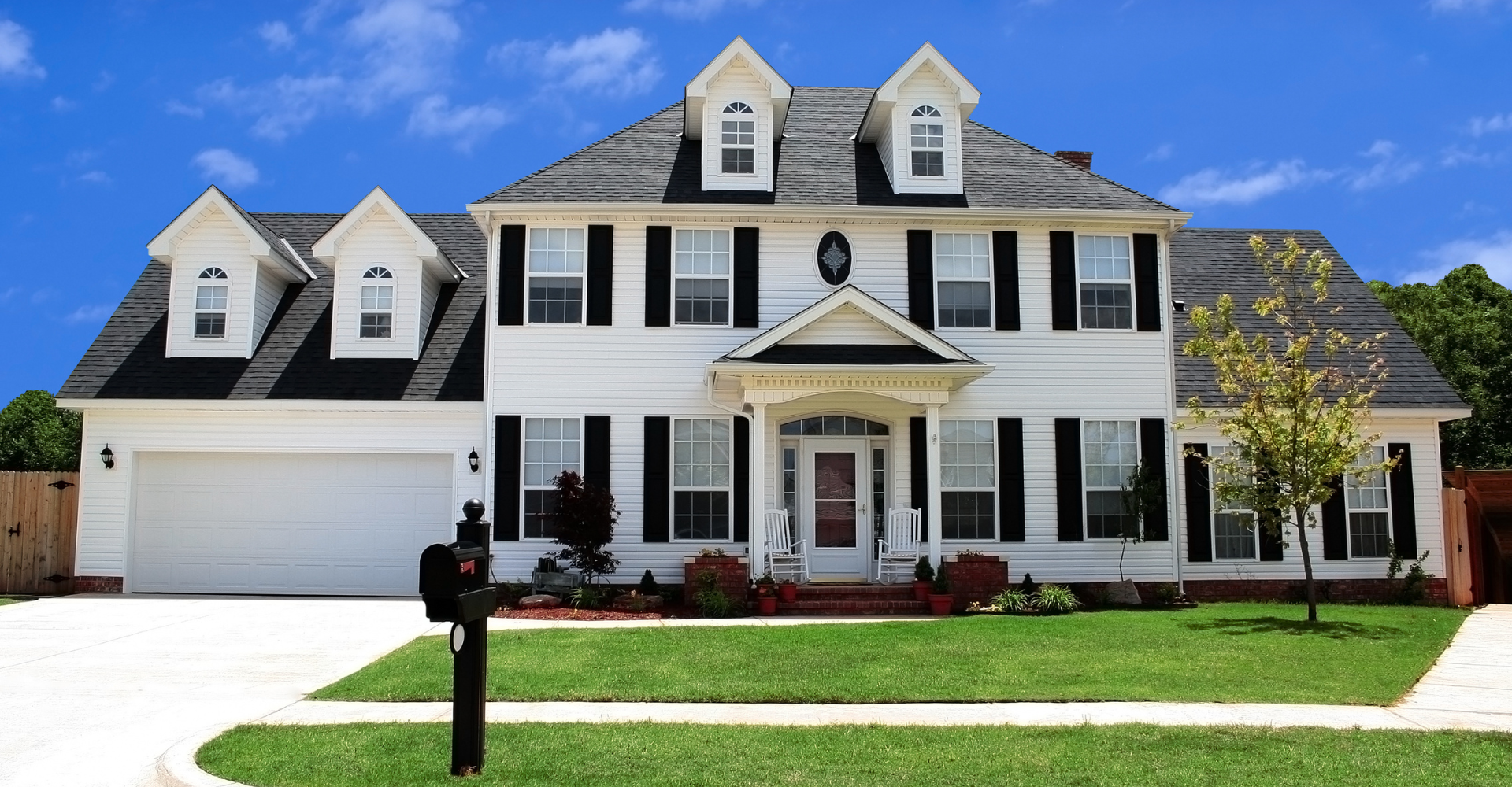 A large white house with black shutters and a mailbox in front of it