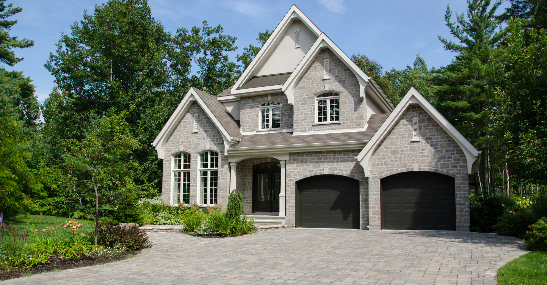 A large house with two garages is surrounded by trees.