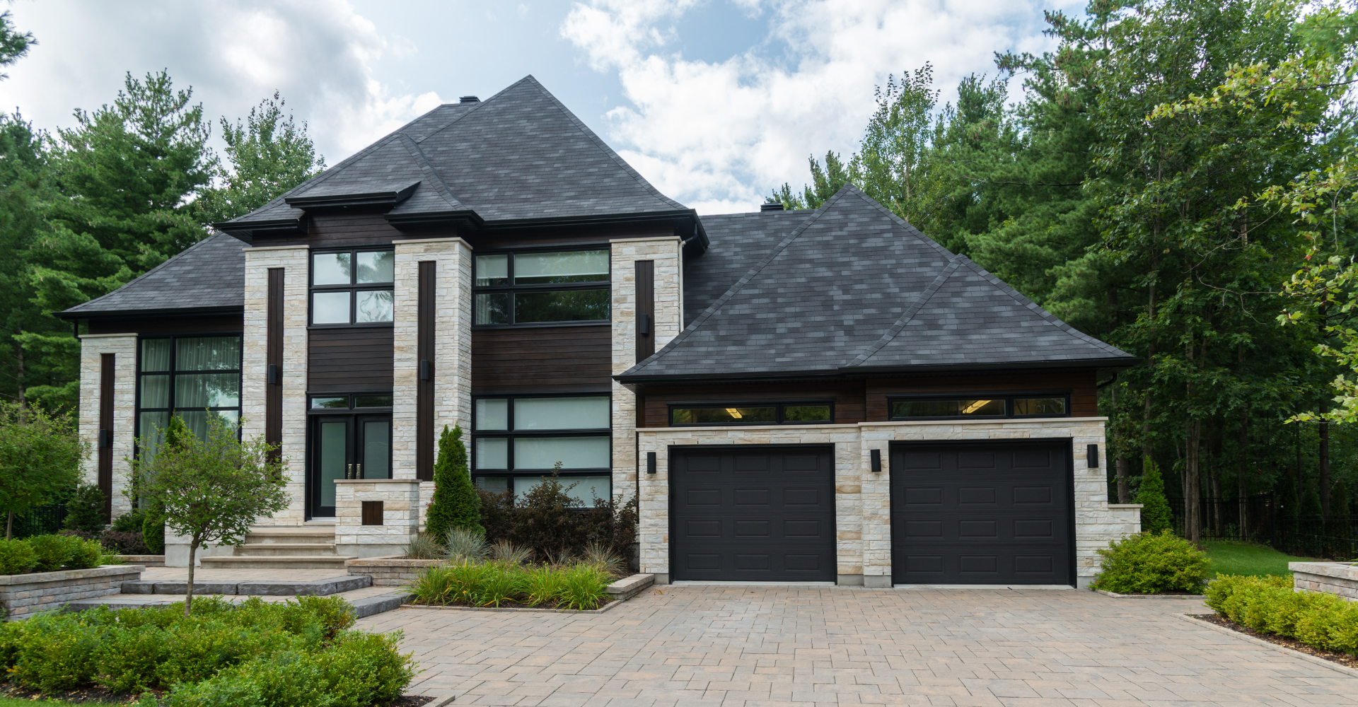 A large house with two black garage doors is surrounded by trees.