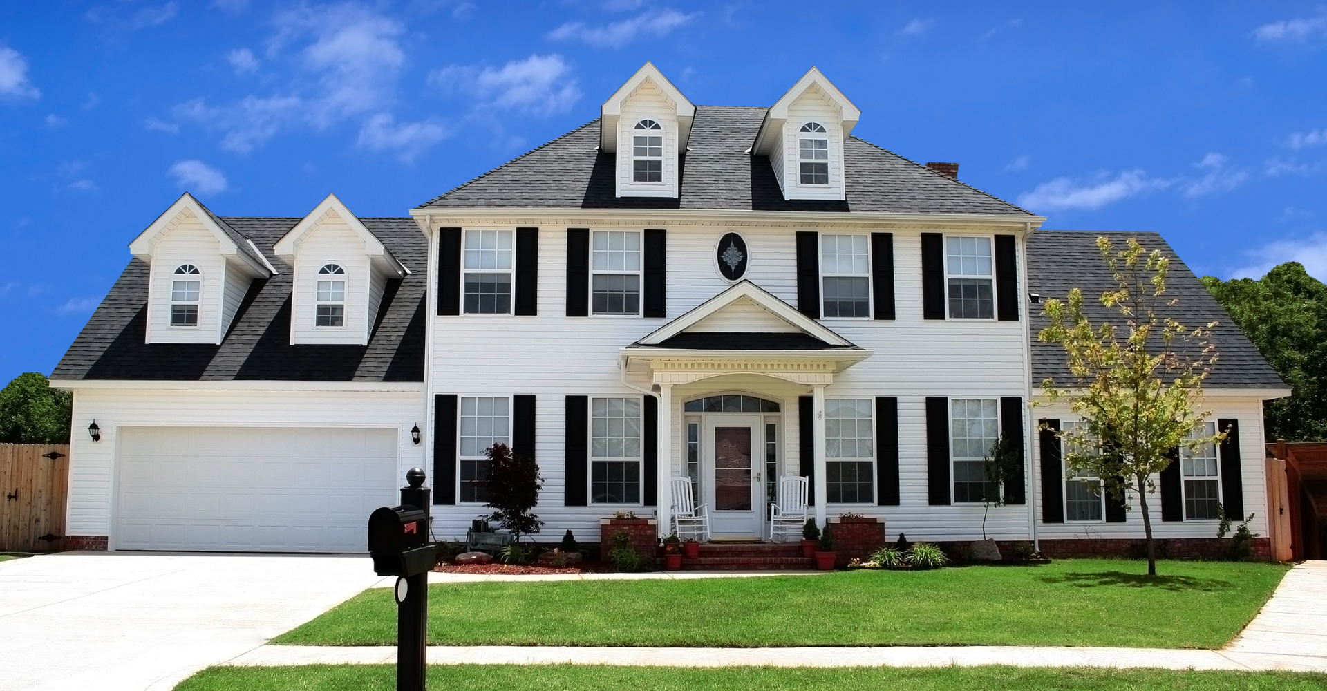 A large white house with black shutters and a mailbox in front of it