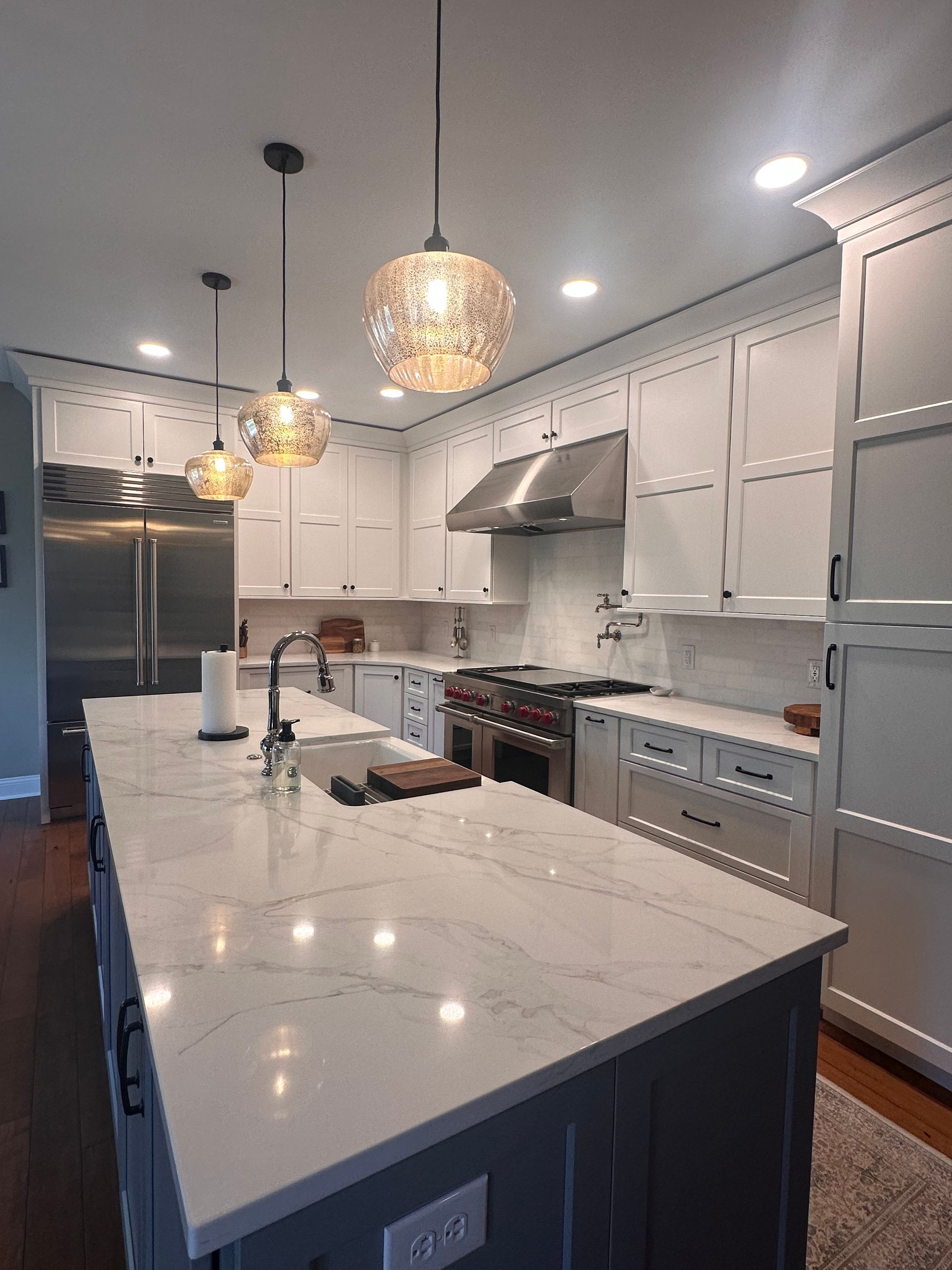 A kitchen with white cabinets and stainless steel appliances and a large island in the middle.