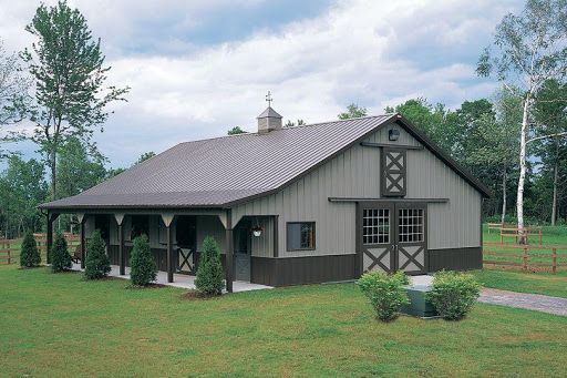 A large barn with a porch is sitting in the middle of a grassy field.