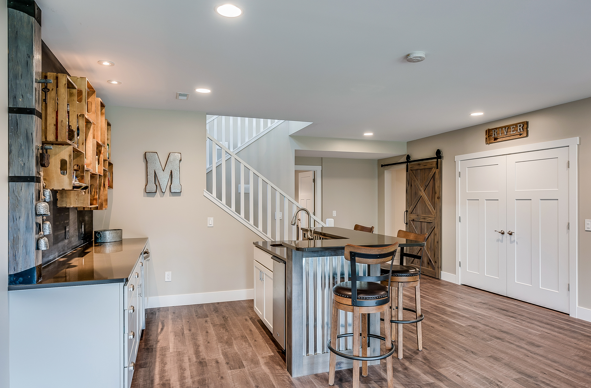 Basement remodeled by compass construction turning it into a modern lavish den and bar area with barn style sliding doors, bar stools, and gorgeous staircase