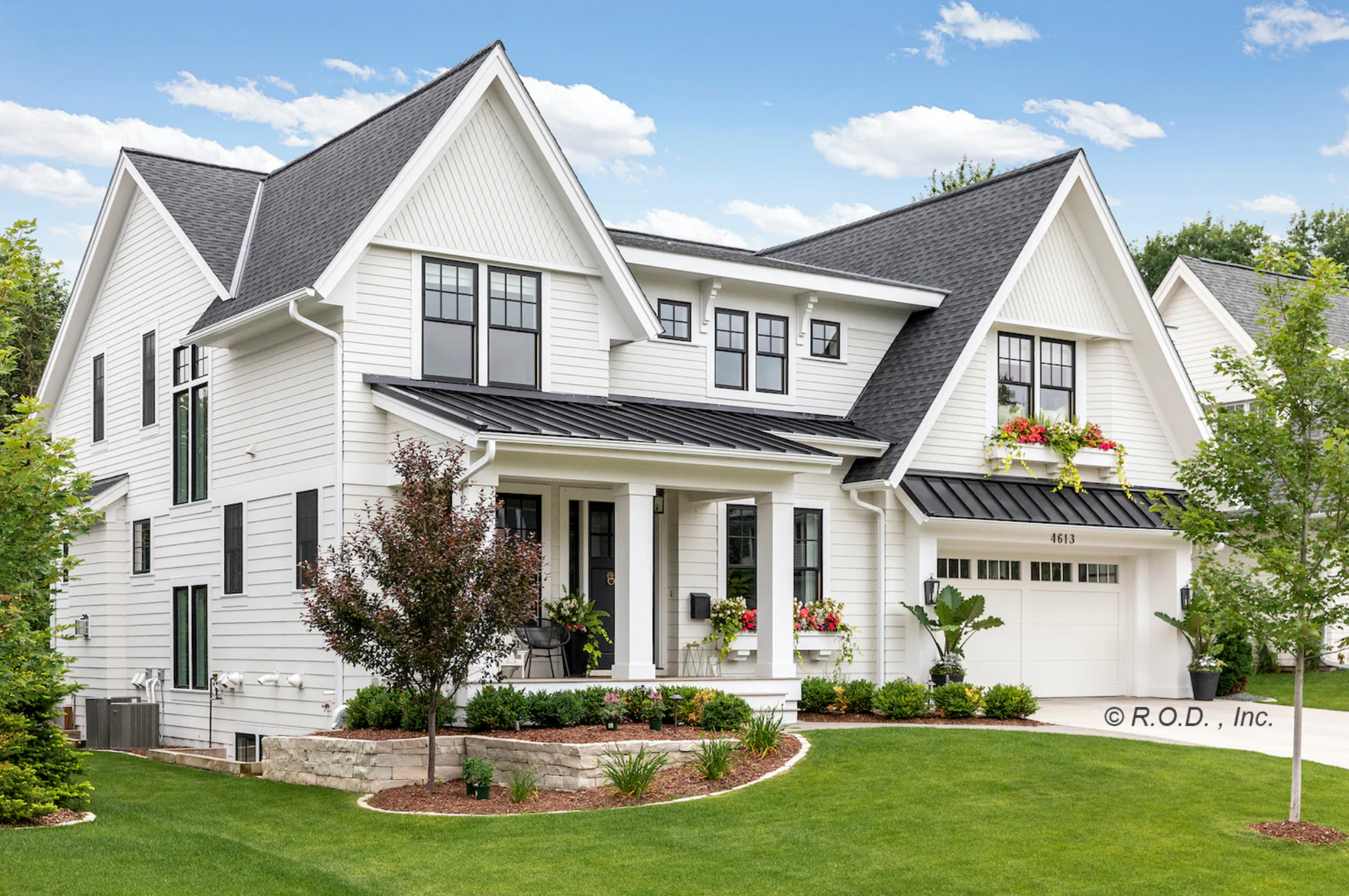 A large white house with a black roof is sitting on top of a lush green lawn.