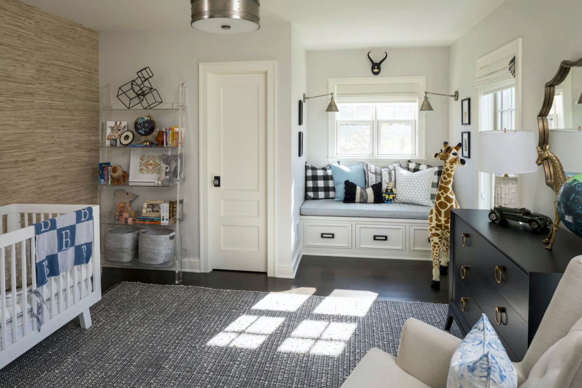 A nursery with a crib , chair , dresser and window seat.