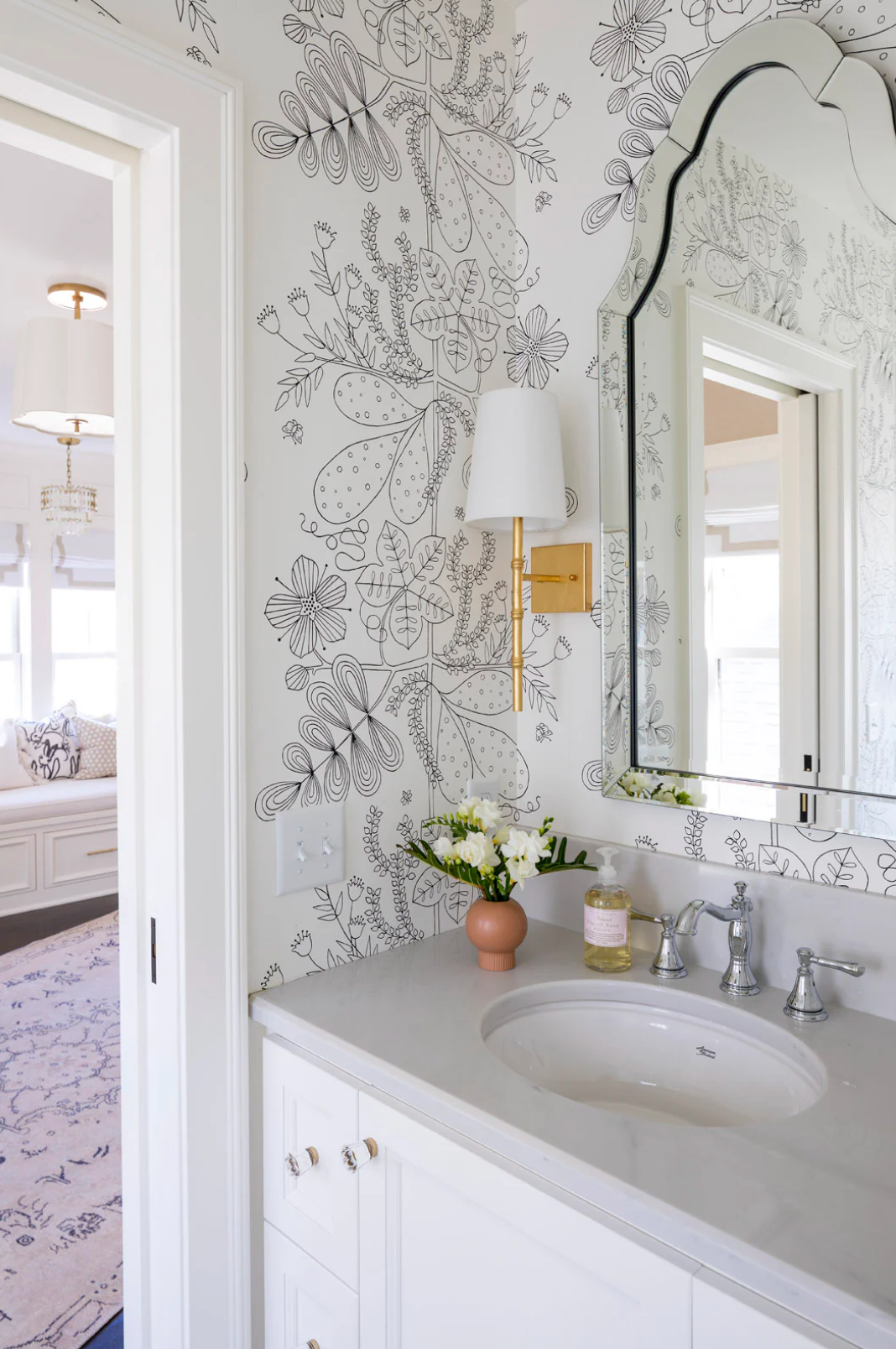 A bathroom with a sink , mirror , and floral wallpaper.