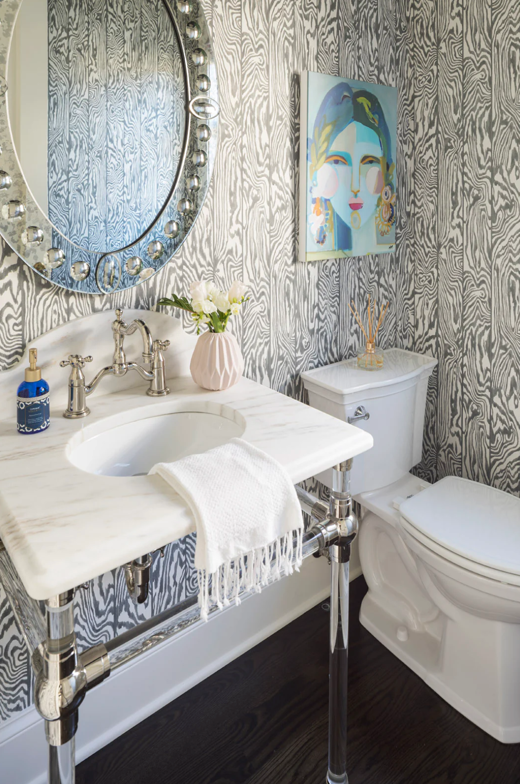 A bathroom with a sink , toilet , mirror and painting on the wall.