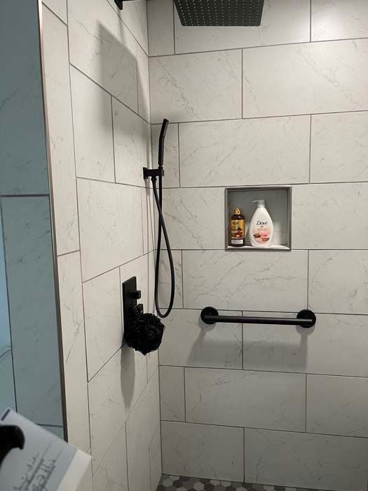 A bathroom with white tiles and a black shower head.