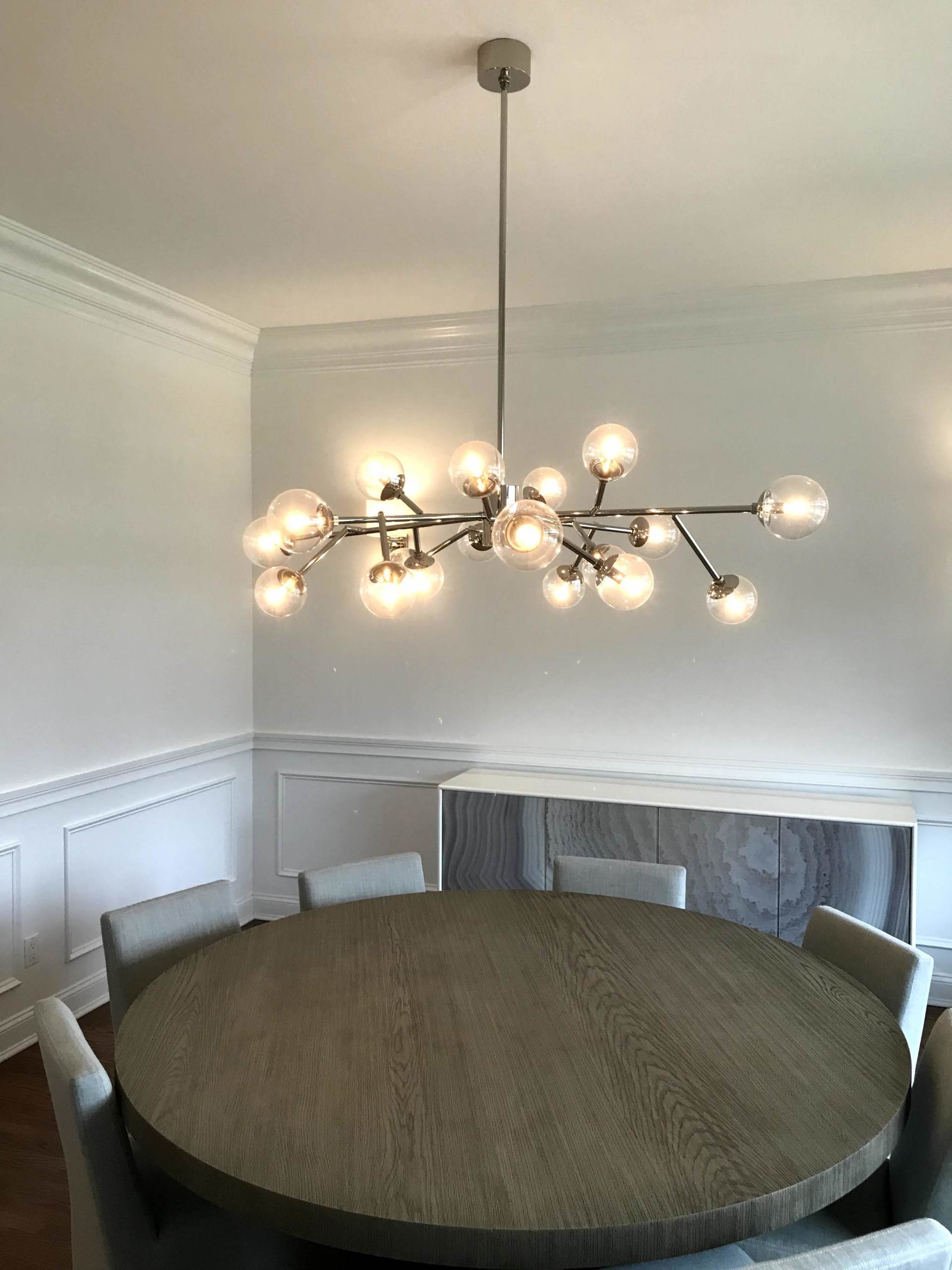 A dining room with a round table and chairs and a chandelier hanging from the ceiling.