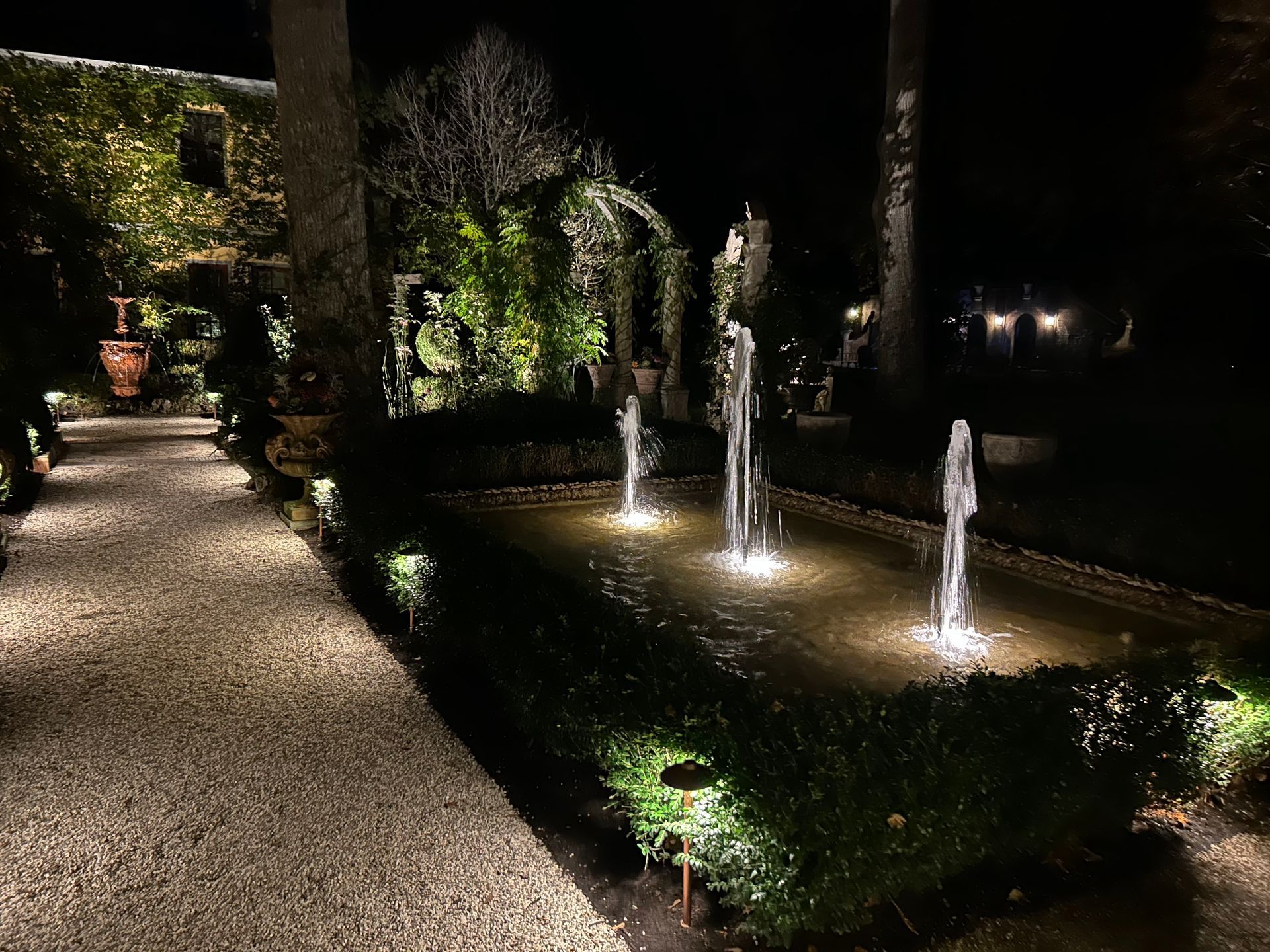 A fountain in a garden is lit up at night.