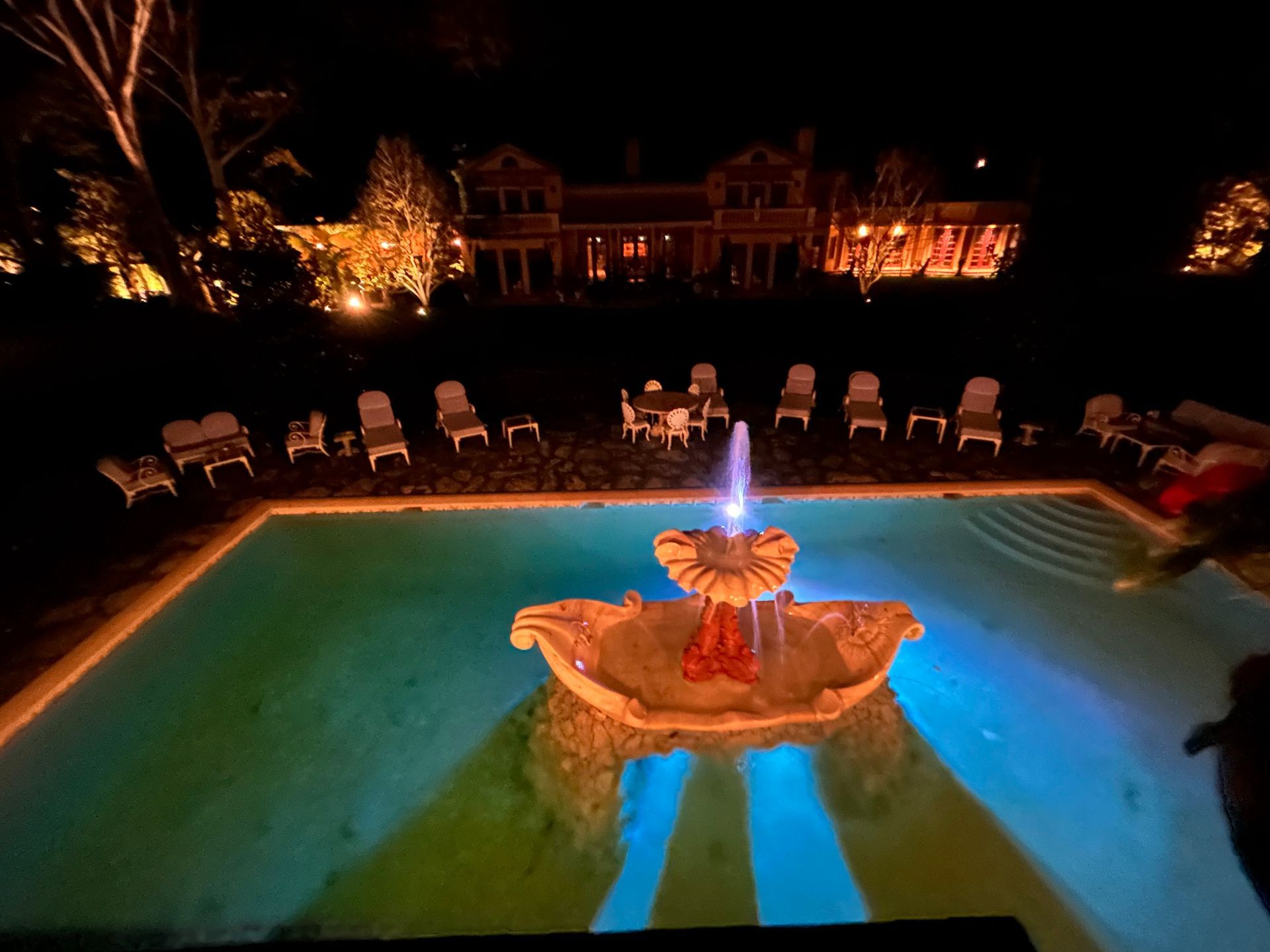 A large swimming pool with a fountain in the middle at night
