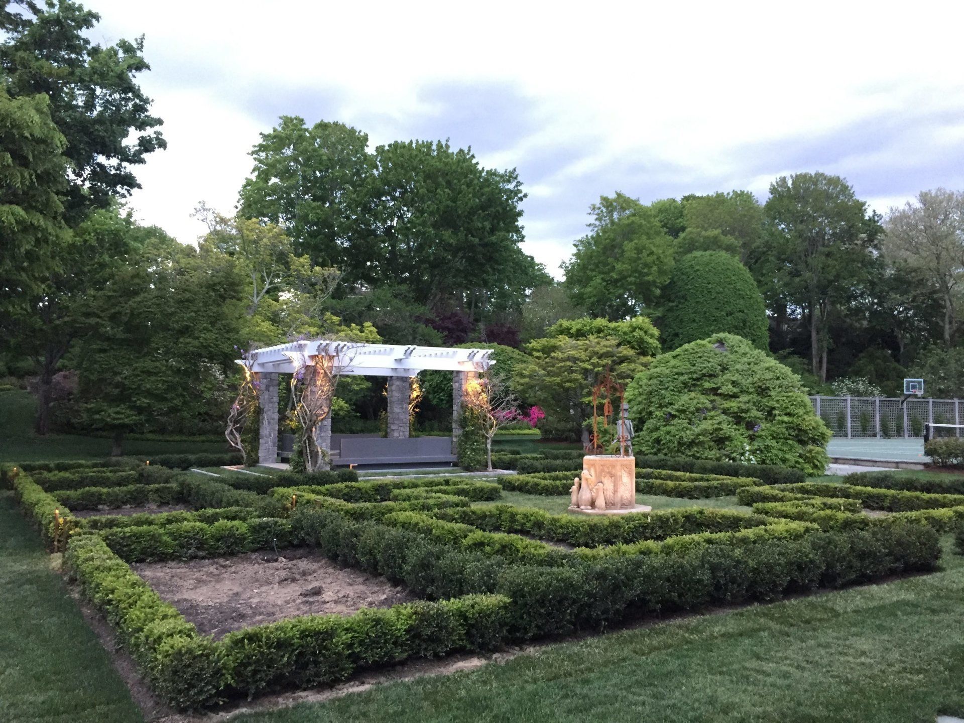There is a gazebo in the middle of the garden surrounded by bushes.
