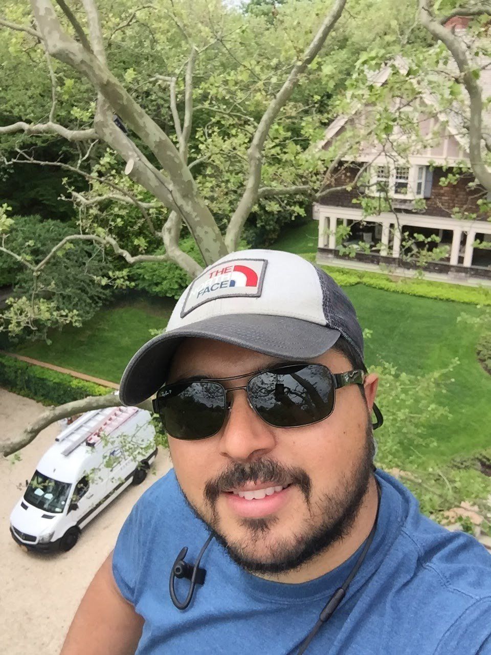 A man wearing a hat and sunglasses is standing in front of a house
