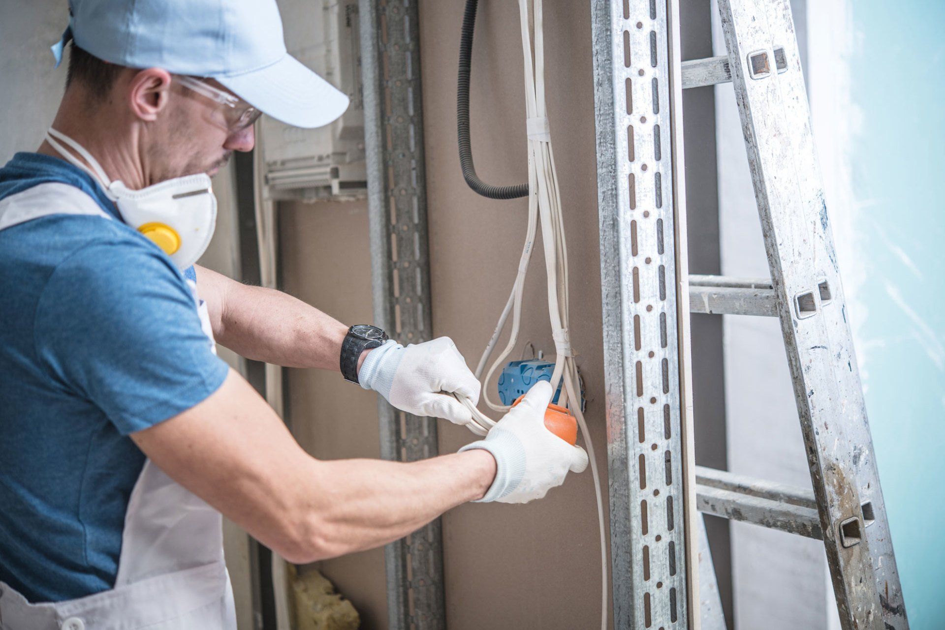 A man wearing a mask and gloves is working on an electrical outlet.
