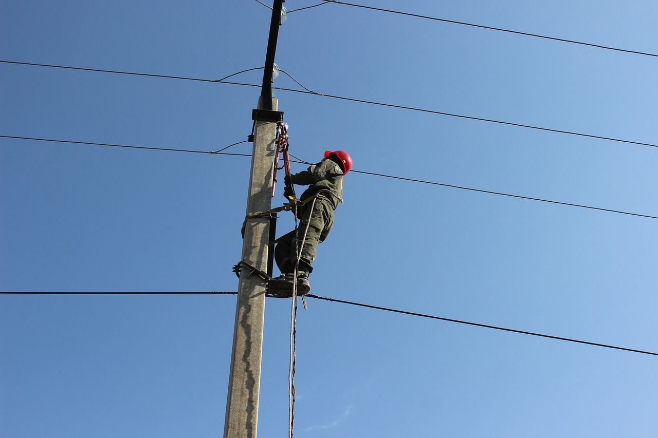 un homme au casque rouge grimpe sur un poteau électrique.