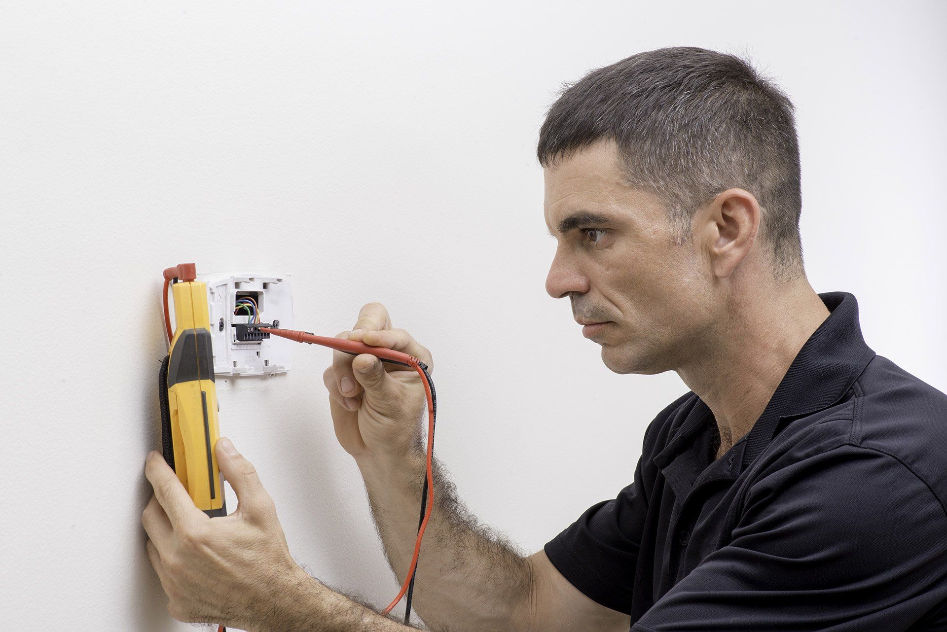 A man is using a multimeter to test an electrical outlet on a wall.