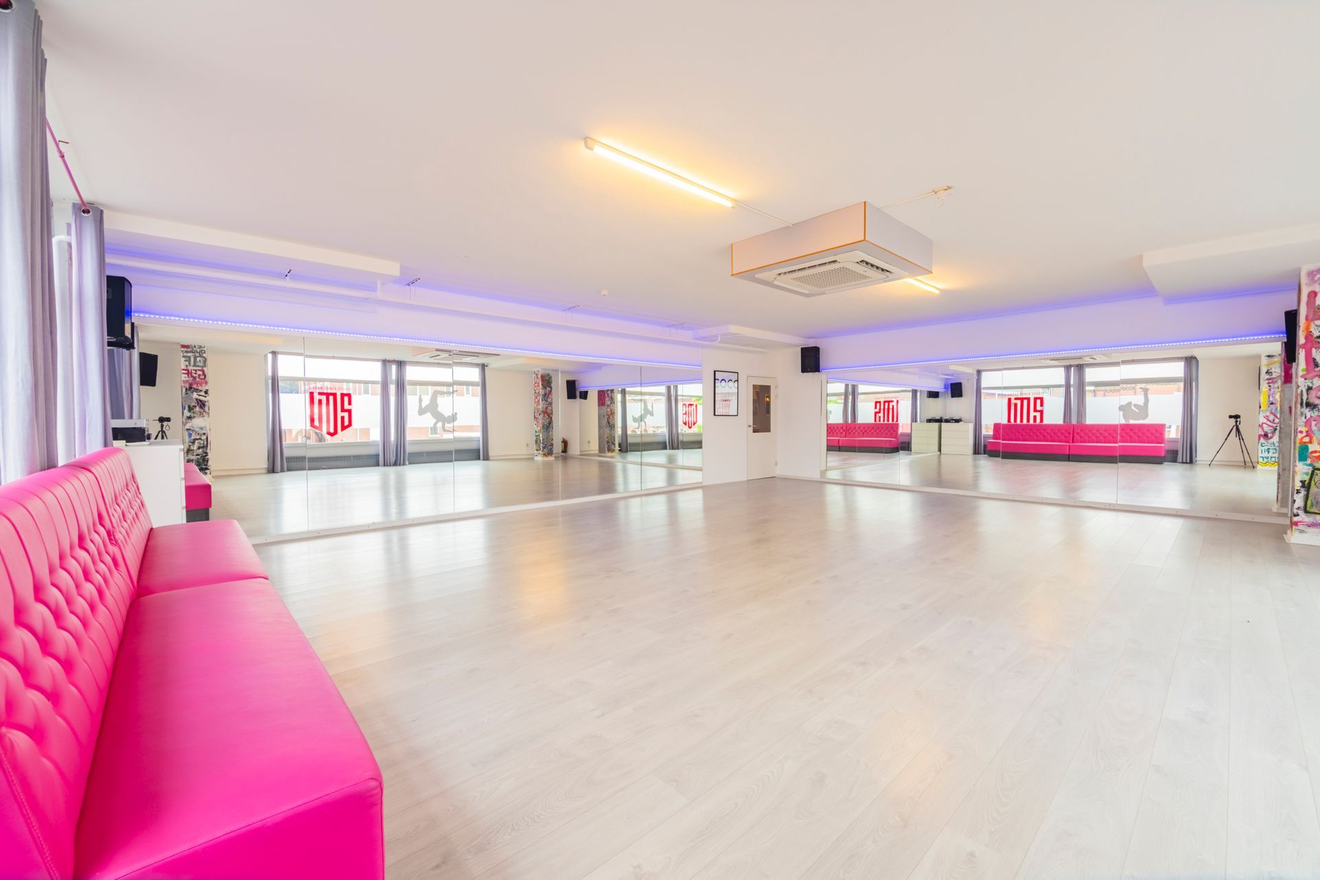 Lichte, lege studio met roze zitmeubels, spiegelwanden en grote ramen.