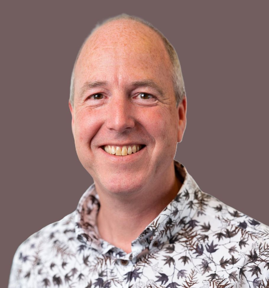 Lachende kale man in een overhemd met patroon tegen een effen grijze achtergrond.