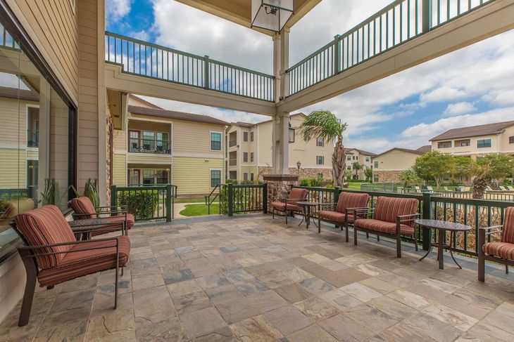 Patio with seating overlooking a courtyard and buildings; cloudy sky.
