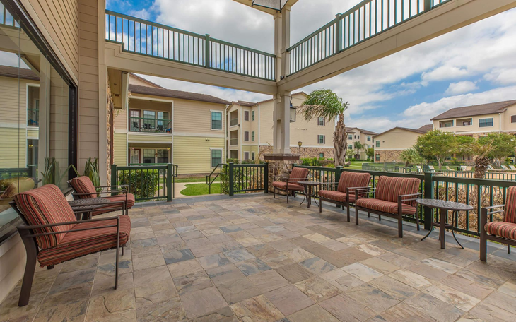 Patio with seating overlooking a courtyard and buildings; cloudy sky.