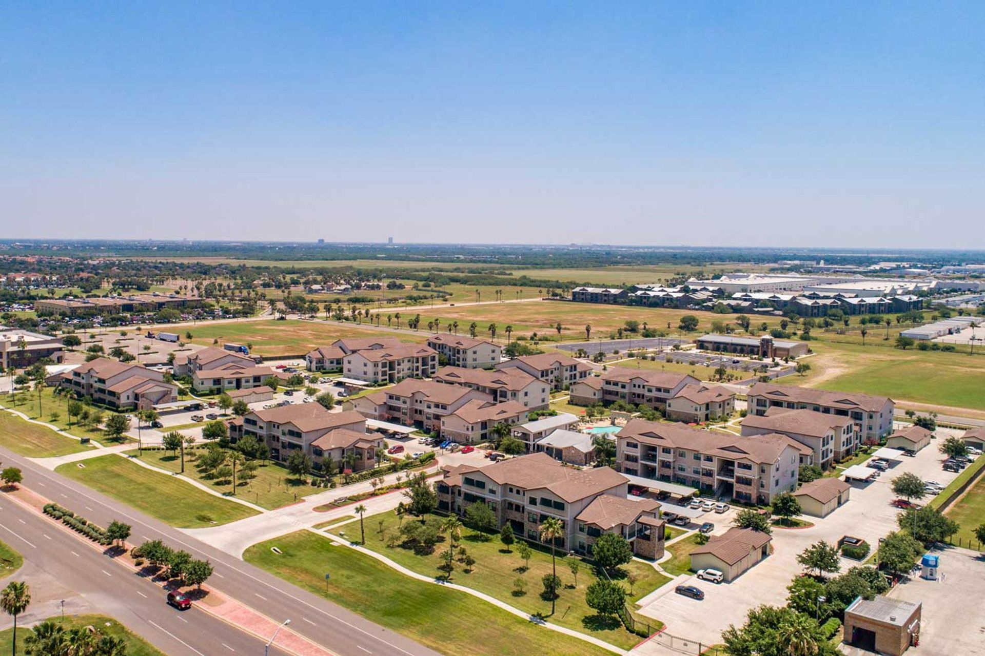 Aerial view of a modern apartment complex with brown roofs, green lawns, and a clear blue sky.