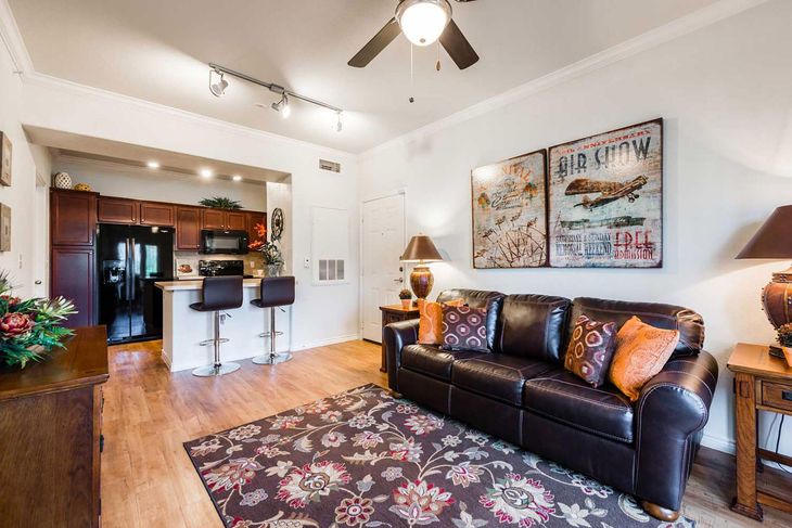 Living room with brown leather sofa, rug, open kitchen with bar stools, and artwork.