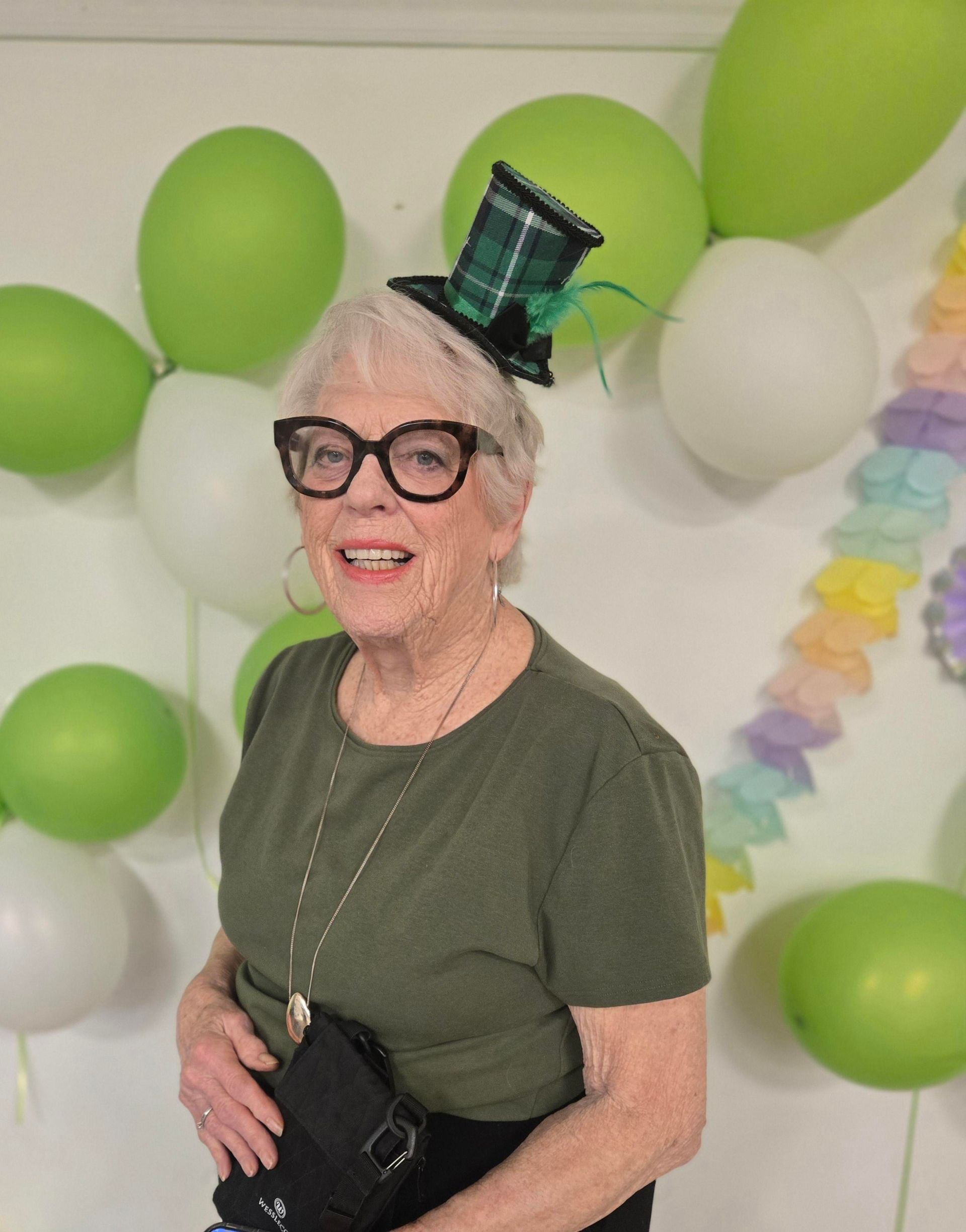Woman in red outfit and heart-shaped glasses poses in front of a red backdrop with a pink balloon.