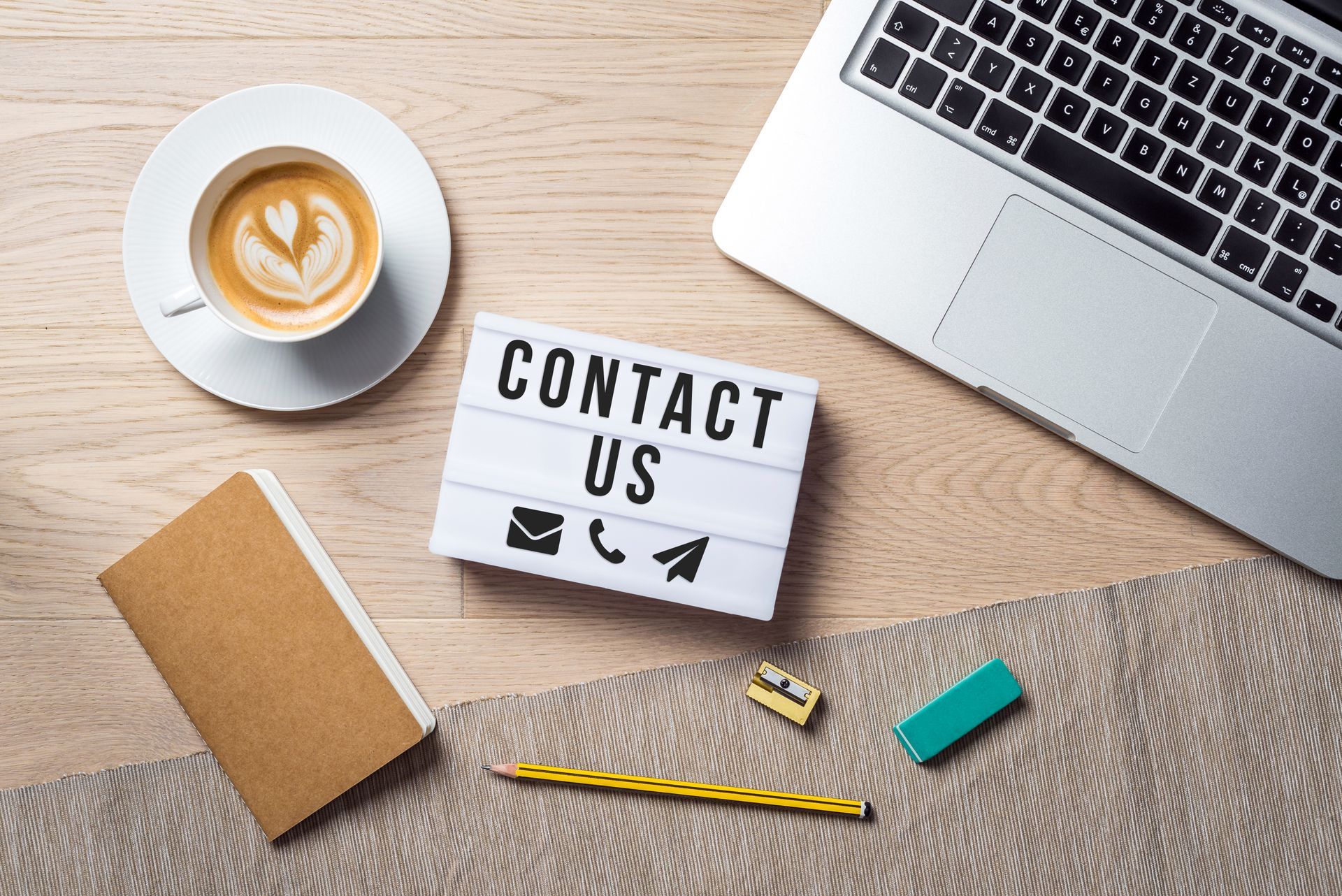 A sign that says contact us is on a wooden table next to a laptop and a cup of coffee.