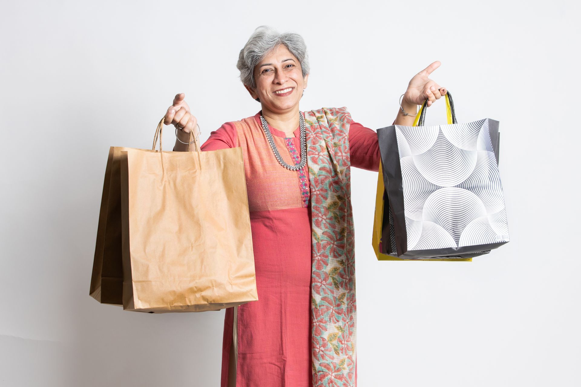 An elderly woman is holding three shopping bags in her hands.