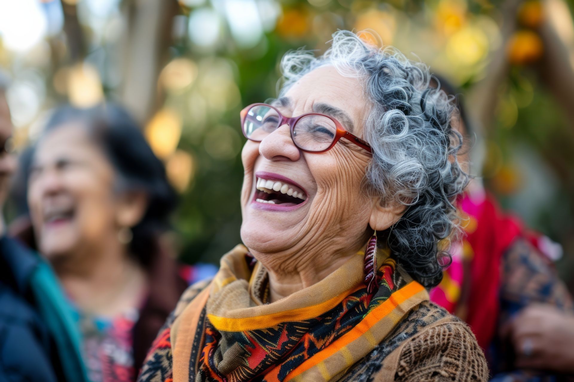 An elderly woman wearing glasses is laughing with a group of people.