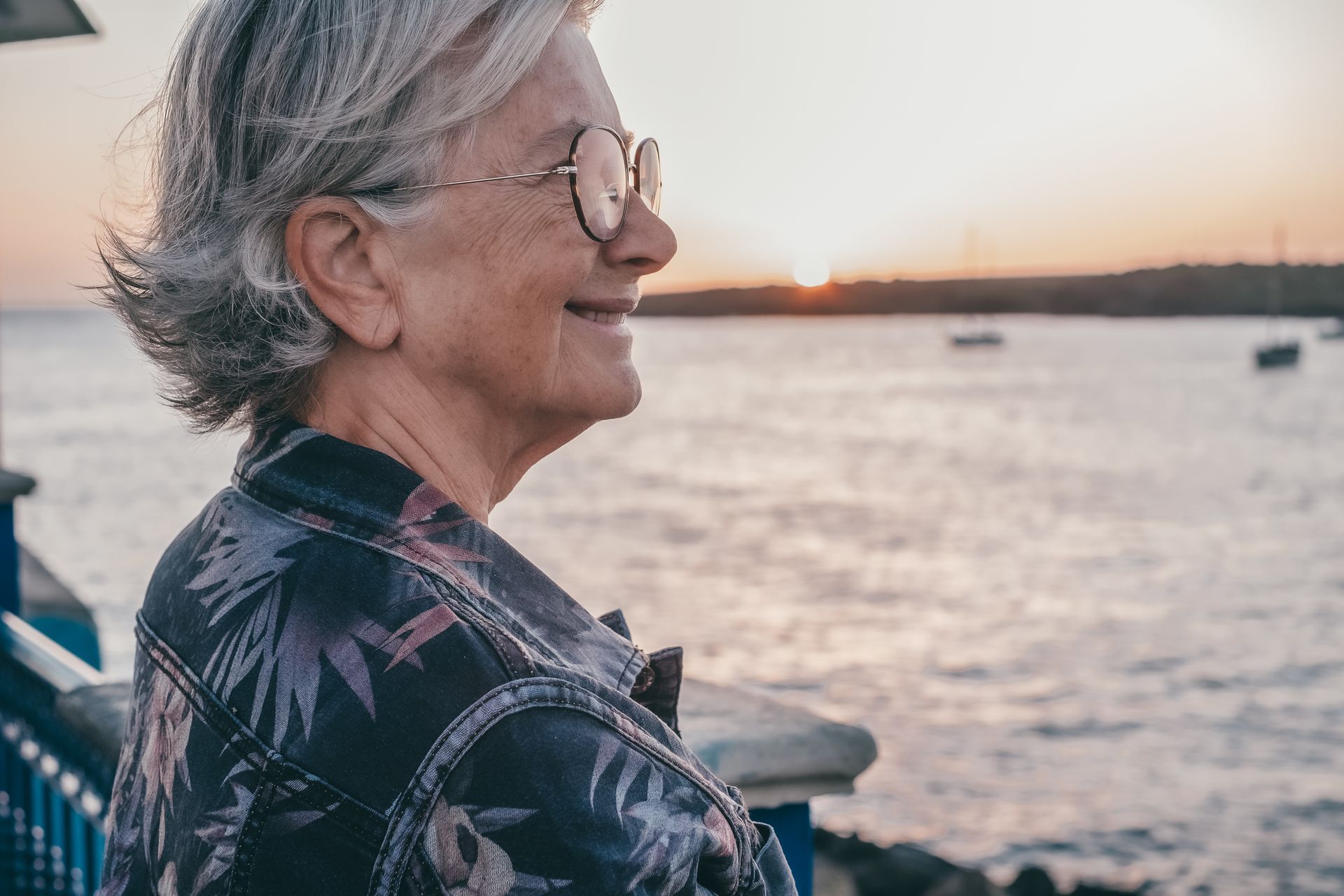 An elderly woman wearing sunglasses is standing next to a body of water.